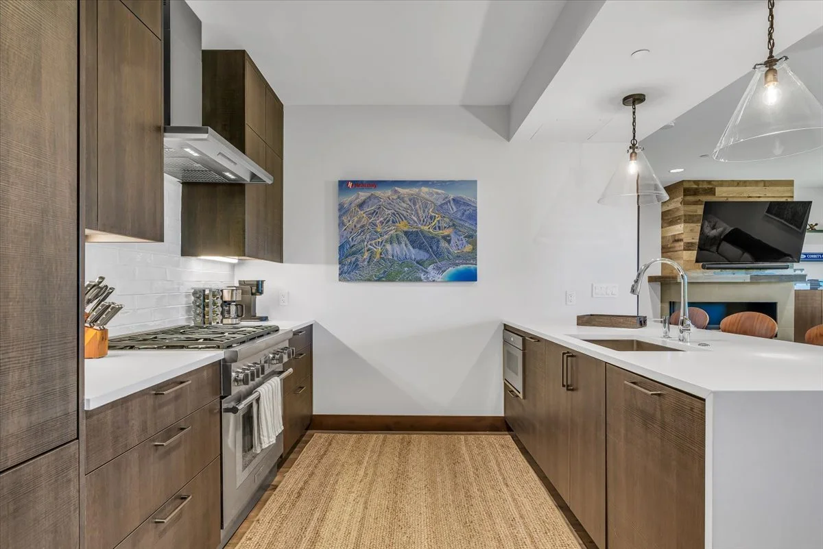 Modern open-concept kitchen featuring sleek wood cabinetry, stainless steel appliances, and a stylish white island with barstool seating. Pendant lighting adds warmth, while a subway tile backsplash and wood flooring create a sophisticated yet inviti
