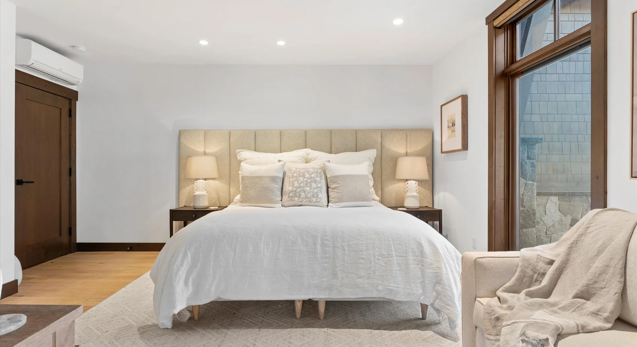 One of Residence 111's three bedrooms, serenely decorated, showcasing a cozy bed, a practical desk, a mounted television and doors leading out to a private patio.
