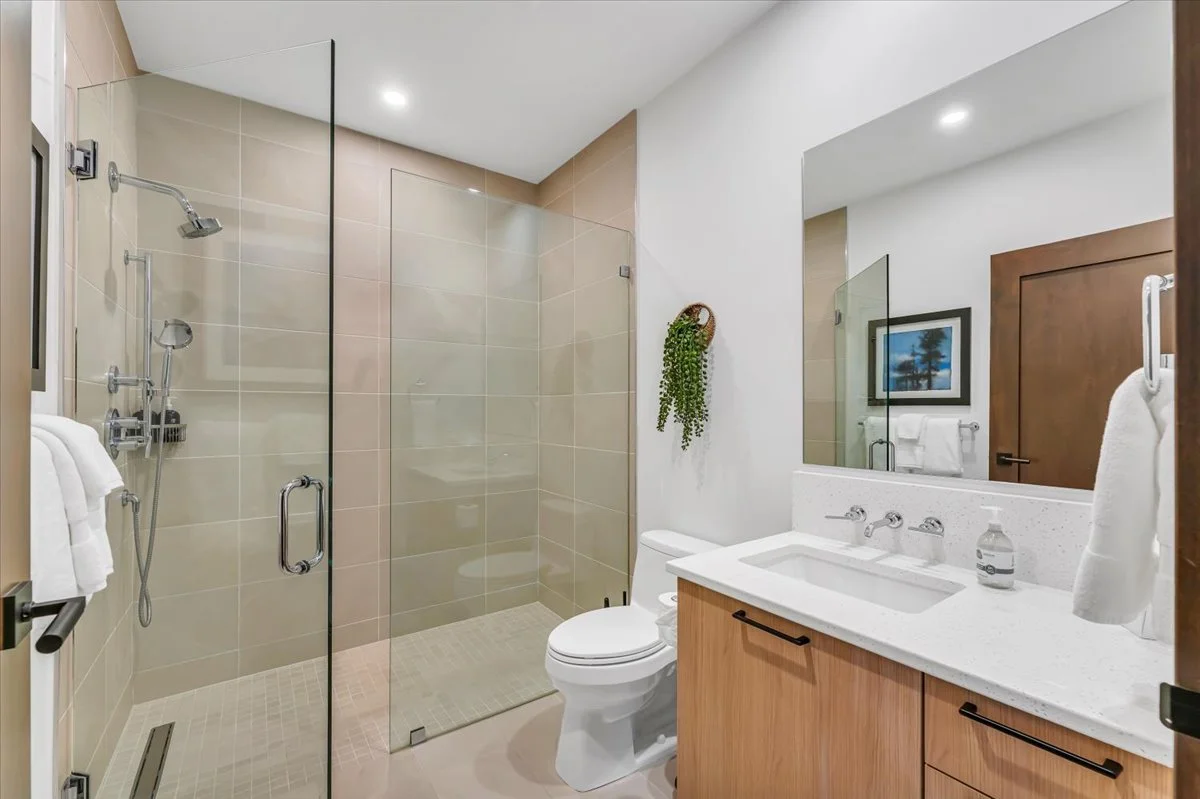 This elegant and artfully designed bathroom features a shower with a glass door, paired with sophisticated stone-tiled flooring. A double vanity with modern cabinetry and a large mirror further enhance the room's refined aesthetic.