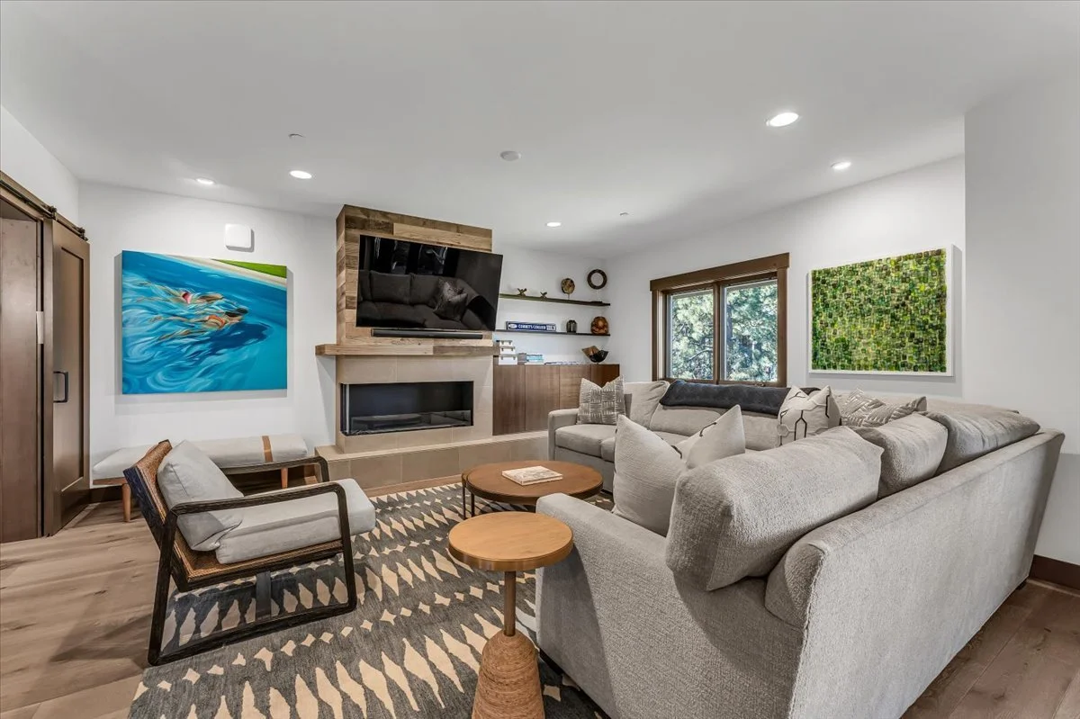 This contemporary open-concept living and kitchen area boasts a spacious seating arrangement, a warm stone fireplace, and rich hardwood floors accented by a stylish area rug. A bedroom, seamlessly integrated into the layout with modern barn doors, of