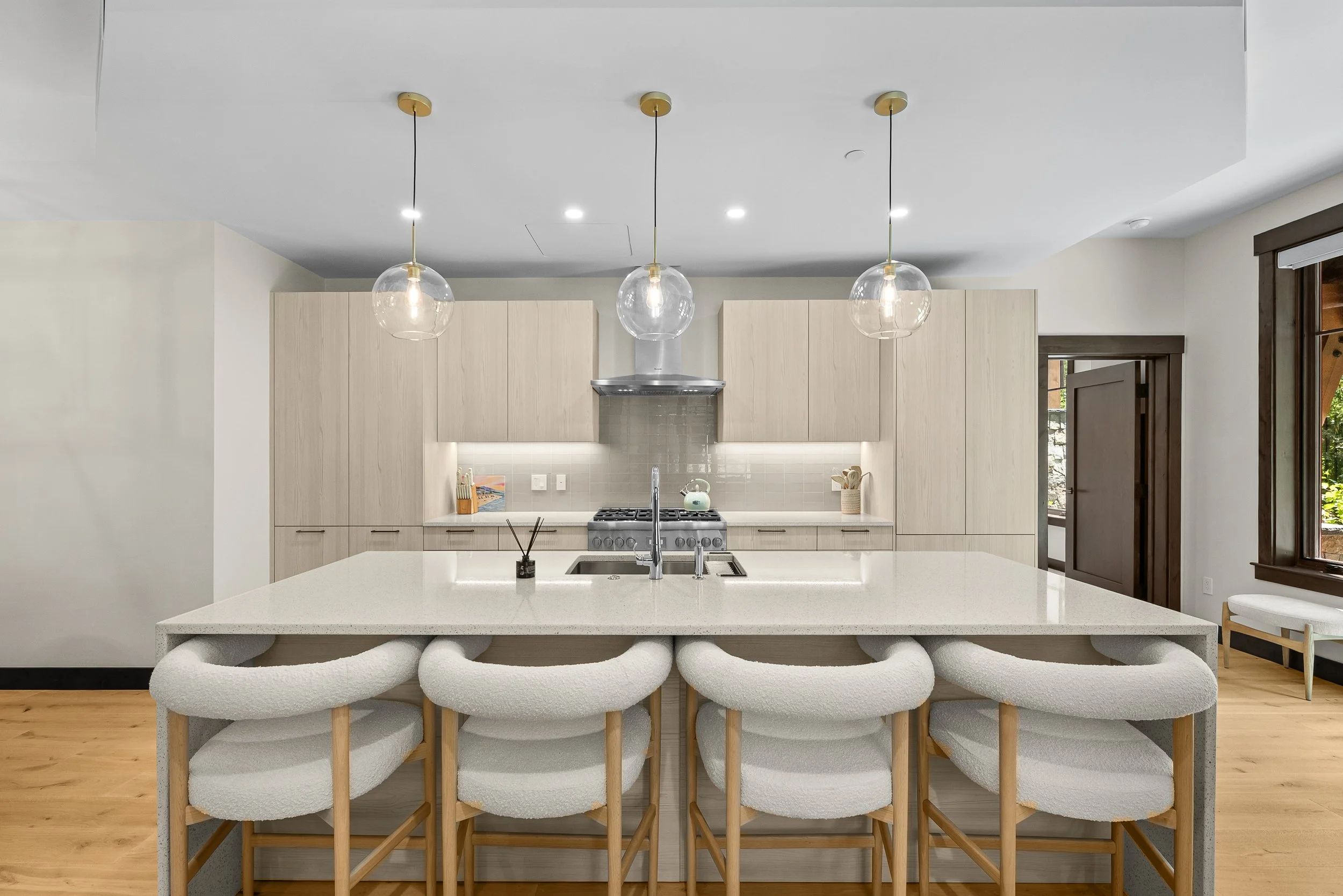A beautifully appointed kitchen at Tahoe Beach Club featuring light wood cabinetry, stone countertops, high-end appliances, and elegant pendant lighting above an island with seating for four.