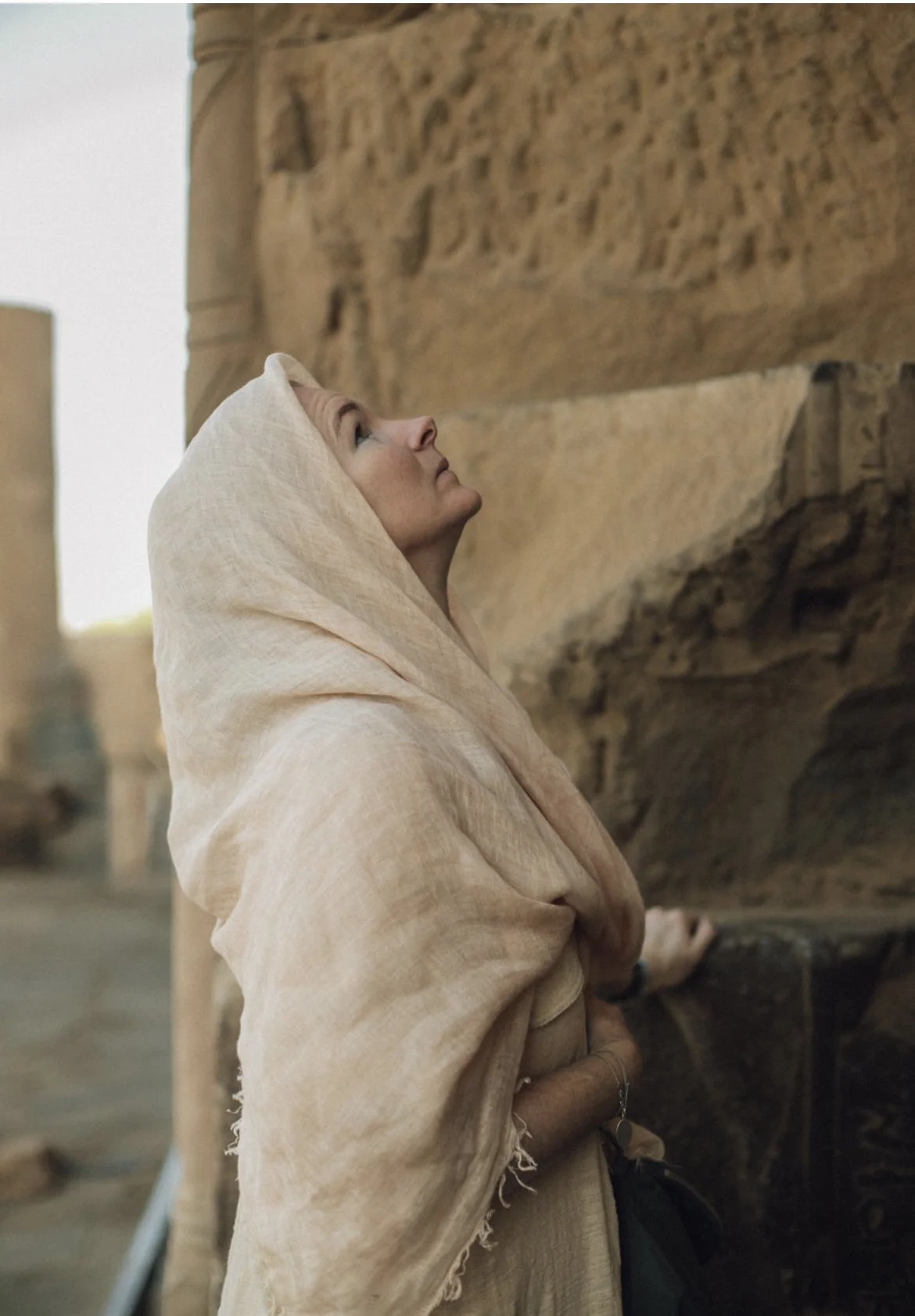 Woman in ivory clothing looking upward beside ancient Egyptian temple carvings.