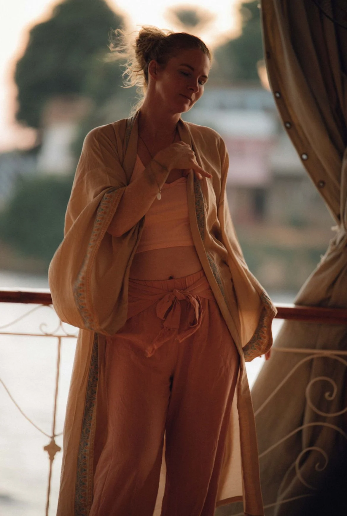 Woman standing on a Nile boat in warm evening light, looking downward in quiet reflection.
