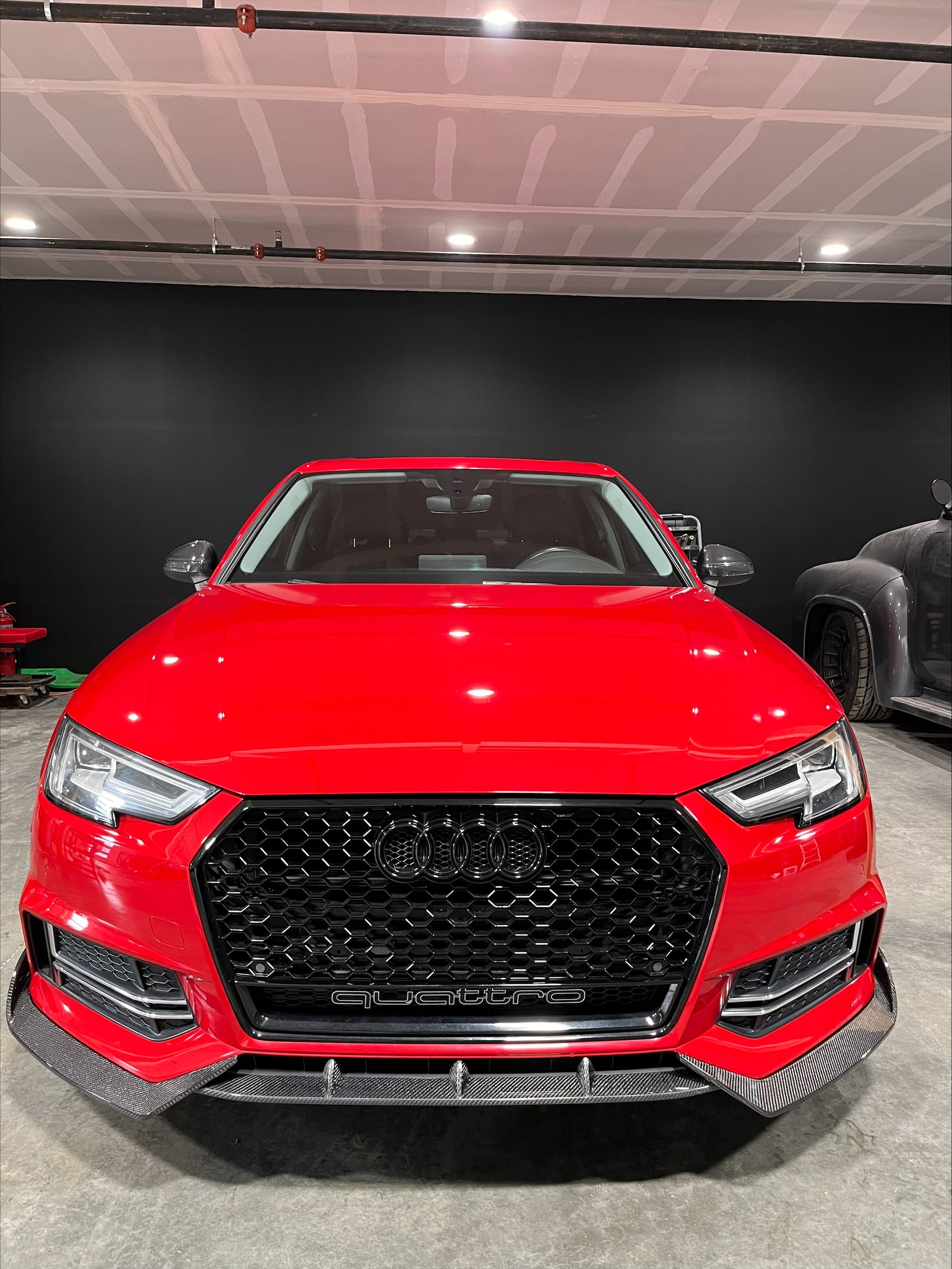 Front view of a red Audi sports car with a honeycomb grille, black accents, and the four-ring logo, parked indoors.