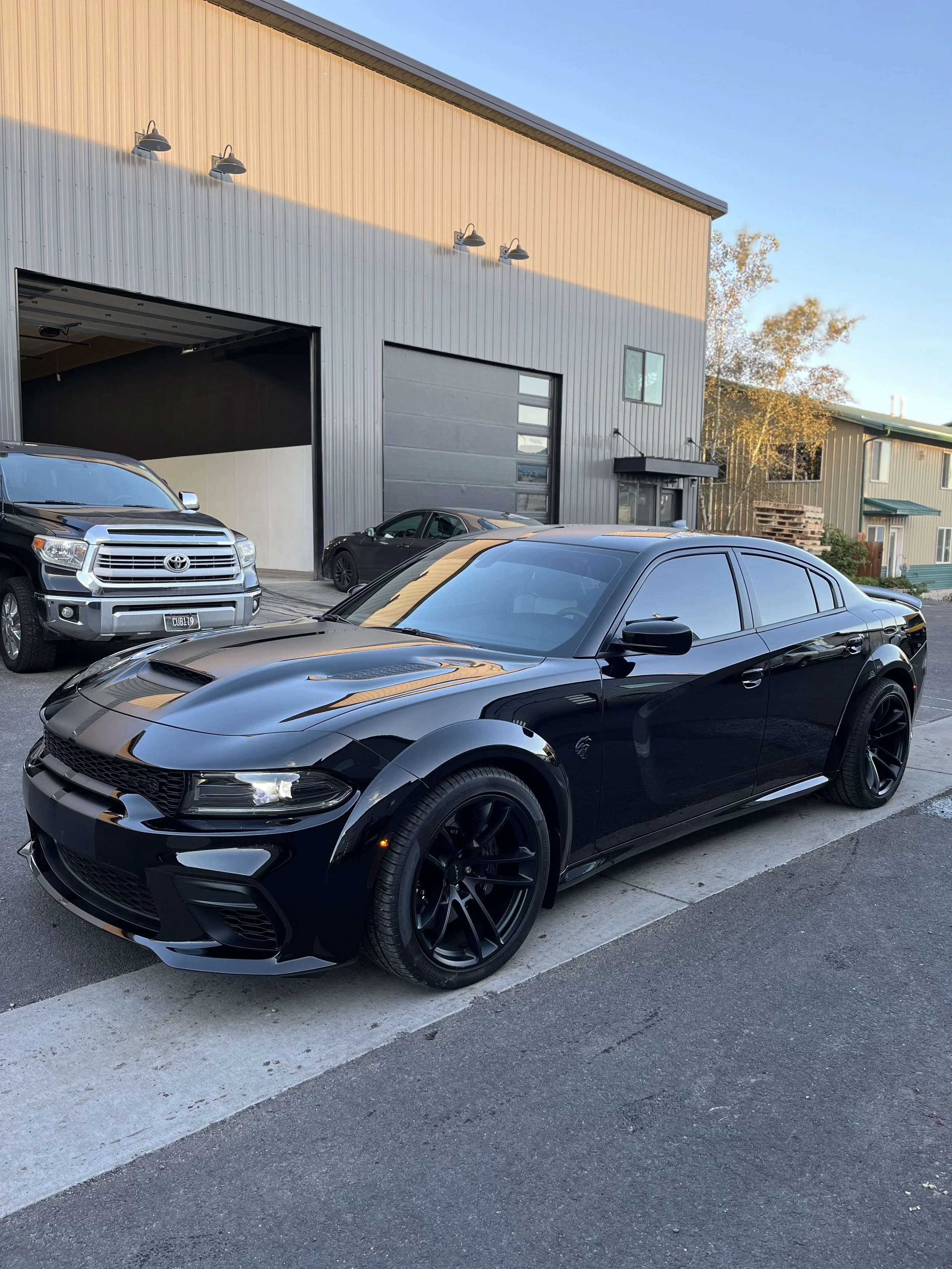 Black sedan car parked outside a building with a grey garage door, alongside a silver pickup truck and a grey sports car.