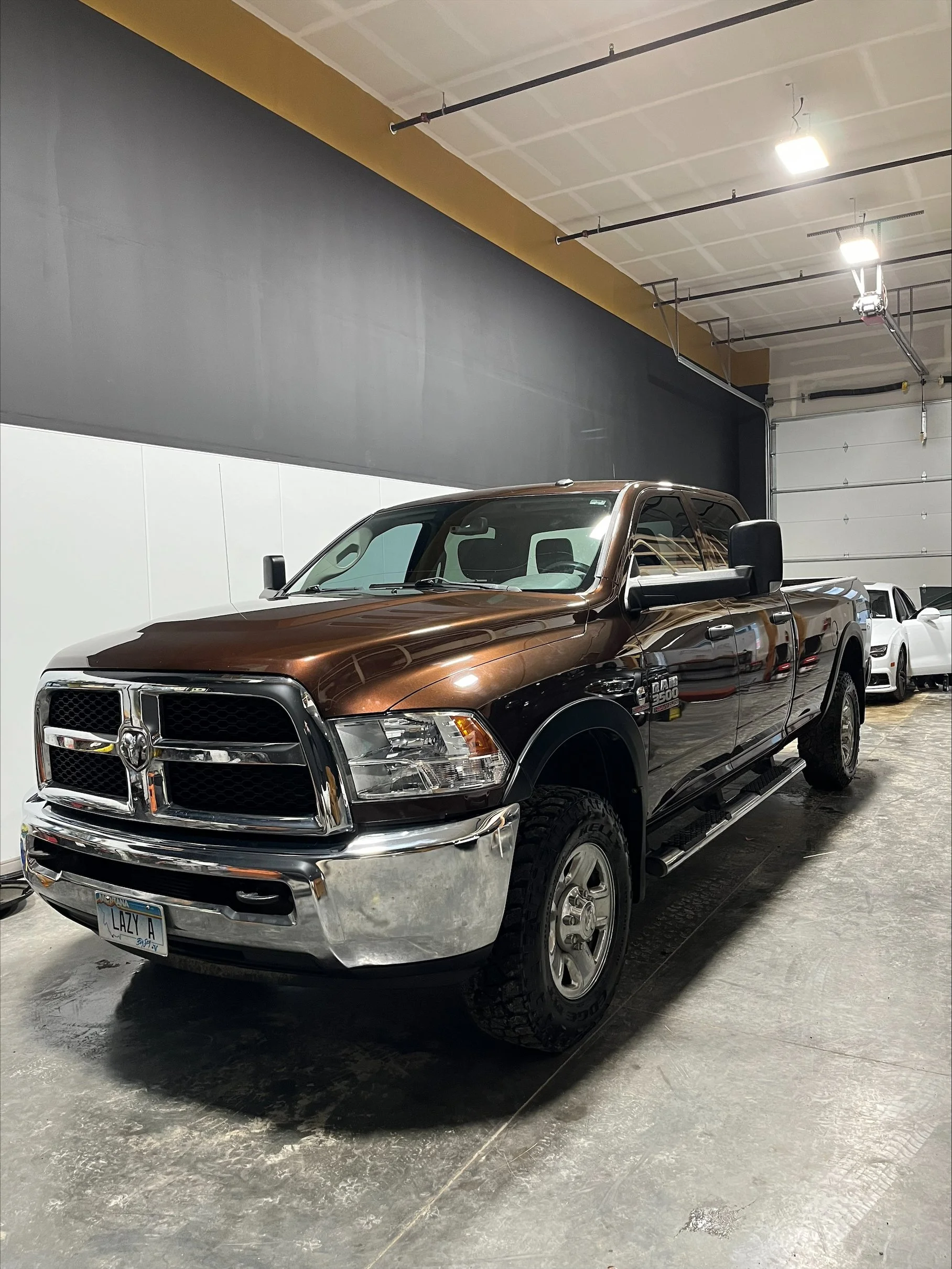 A brown and black RAM 2500 pickup truck parked indoors in a warehouse or garage with other vehicles in the background.