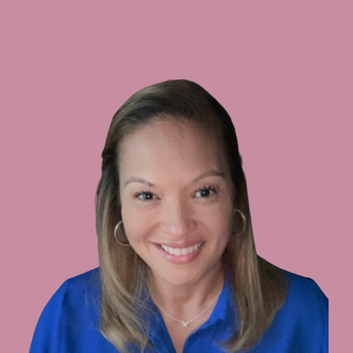 A smiling woman with light brown hair, wearing hoop earrings, a delicate necklace, and a blue blouse, posing indoors.