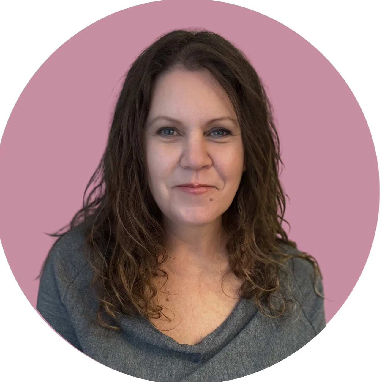 A woman with short brown hair and blue eyes smiling at the camera, wearing a black top, indoors with a blurred background.