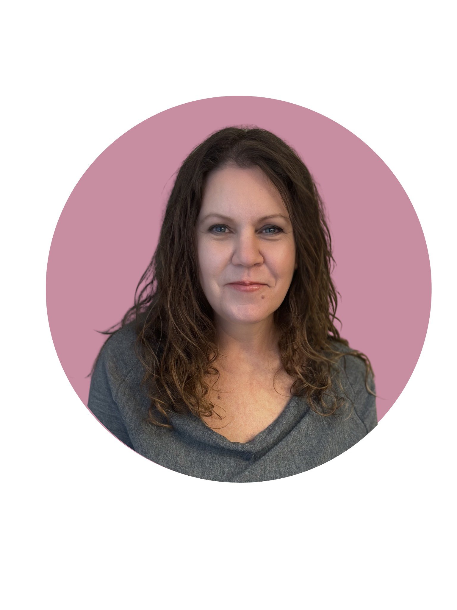 Close-up of a woman with short, curly brown hair, blue eyes, and light skin, smiling slightly, wearing a black top, indoors.