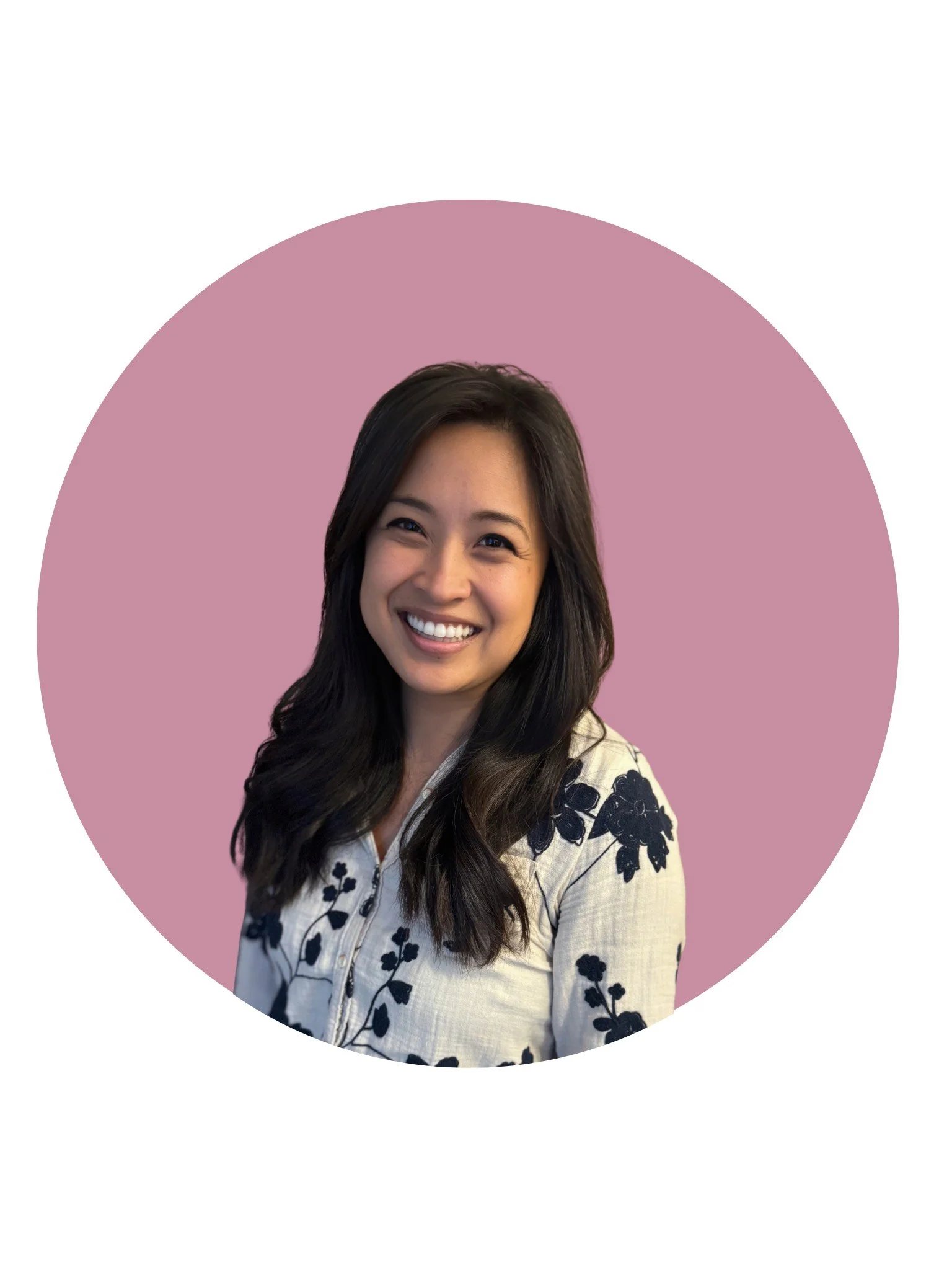 A woman with long, wavy dark hair with lighter highlights, smiling inside a car.