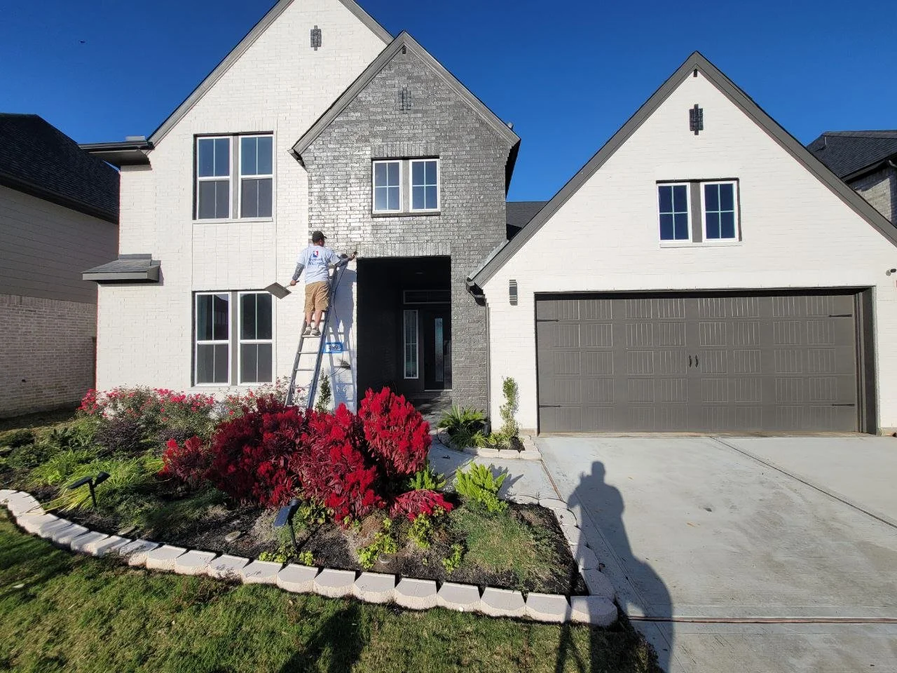 Professional painter on a ladder working on a freshly painted brick exterior in Katy, Texas