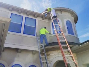 Two professional painters applying paint to a stucco exterior home in Missouri City, Texas