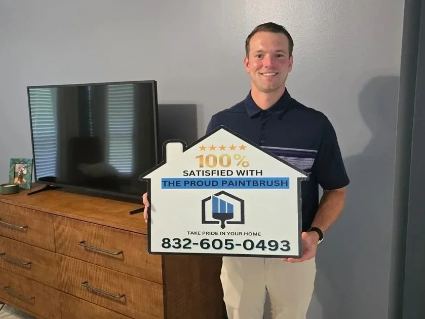 Homeowner in Katy Texas holding a 100 percent satisfied sign in a freshly painted bedroom completed by The Proud Paintbrush