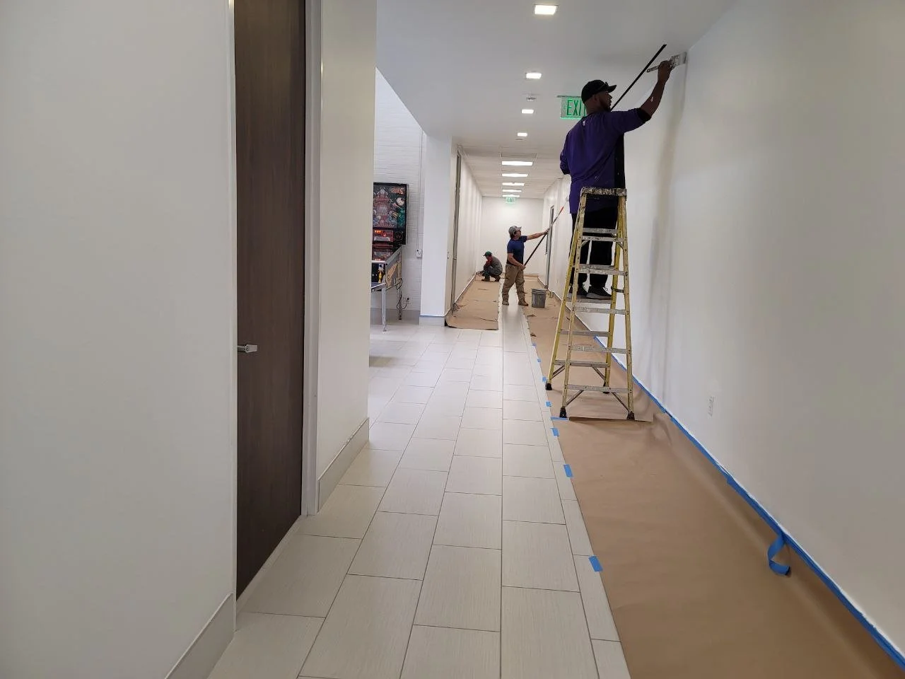 Painters working in a long hallway with floors and baseboards masked during interior painting in Sugar Land, Texas.
