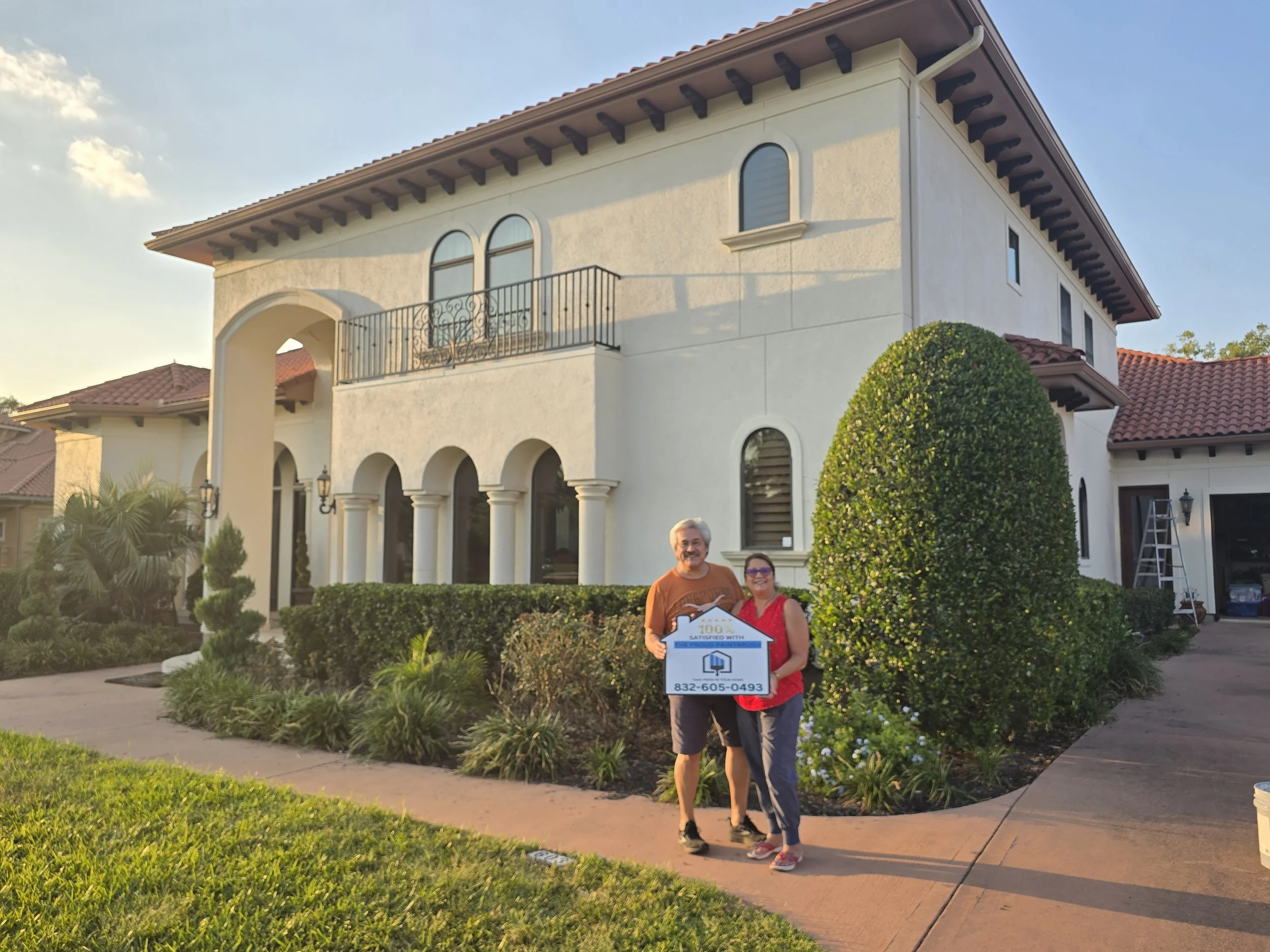 Freshly painted stucco exterior with satisfied homeowners holding sign in Southwest Houston, Texas