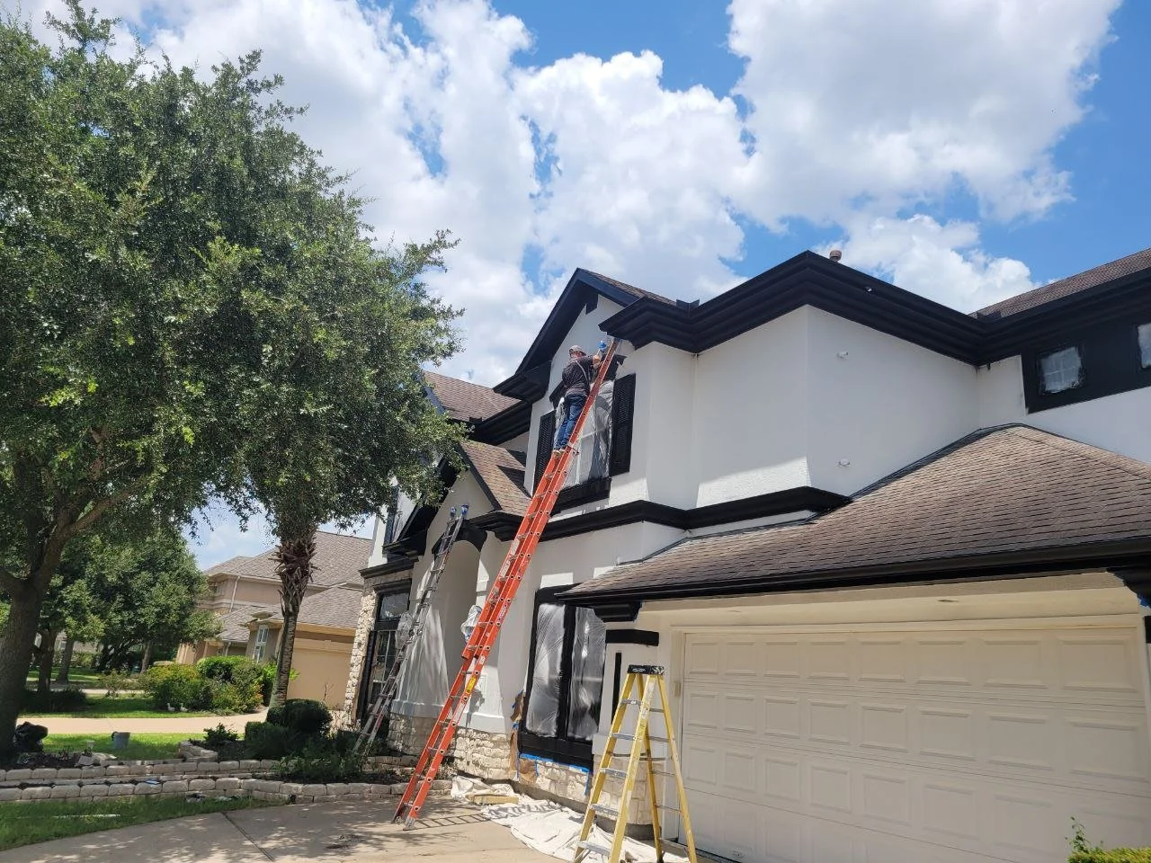 Professional painter on a ladder applying paint to a stucco exterior home in Sugar Land, Texas