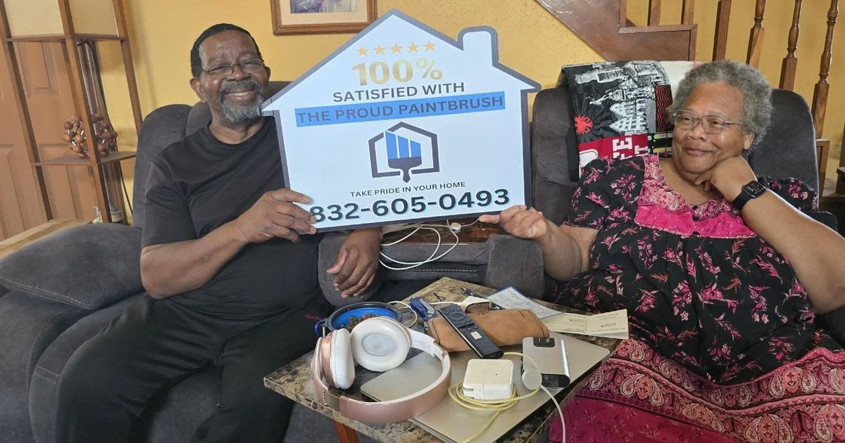 Smiling homeowner holding “100% Satisfied with The Proud Paintbrush” sign in front of freshly painted house in Sugar Land