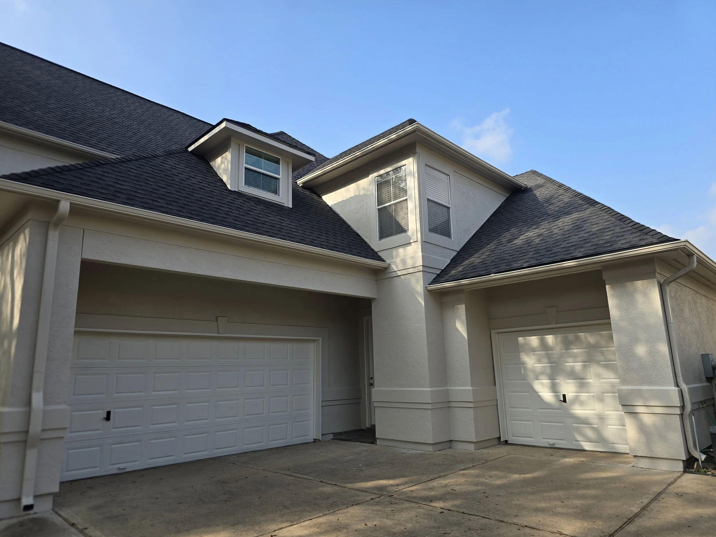 Exterior house painting in Katy, TX featuring freshly painted stucco, trim, and garage doors