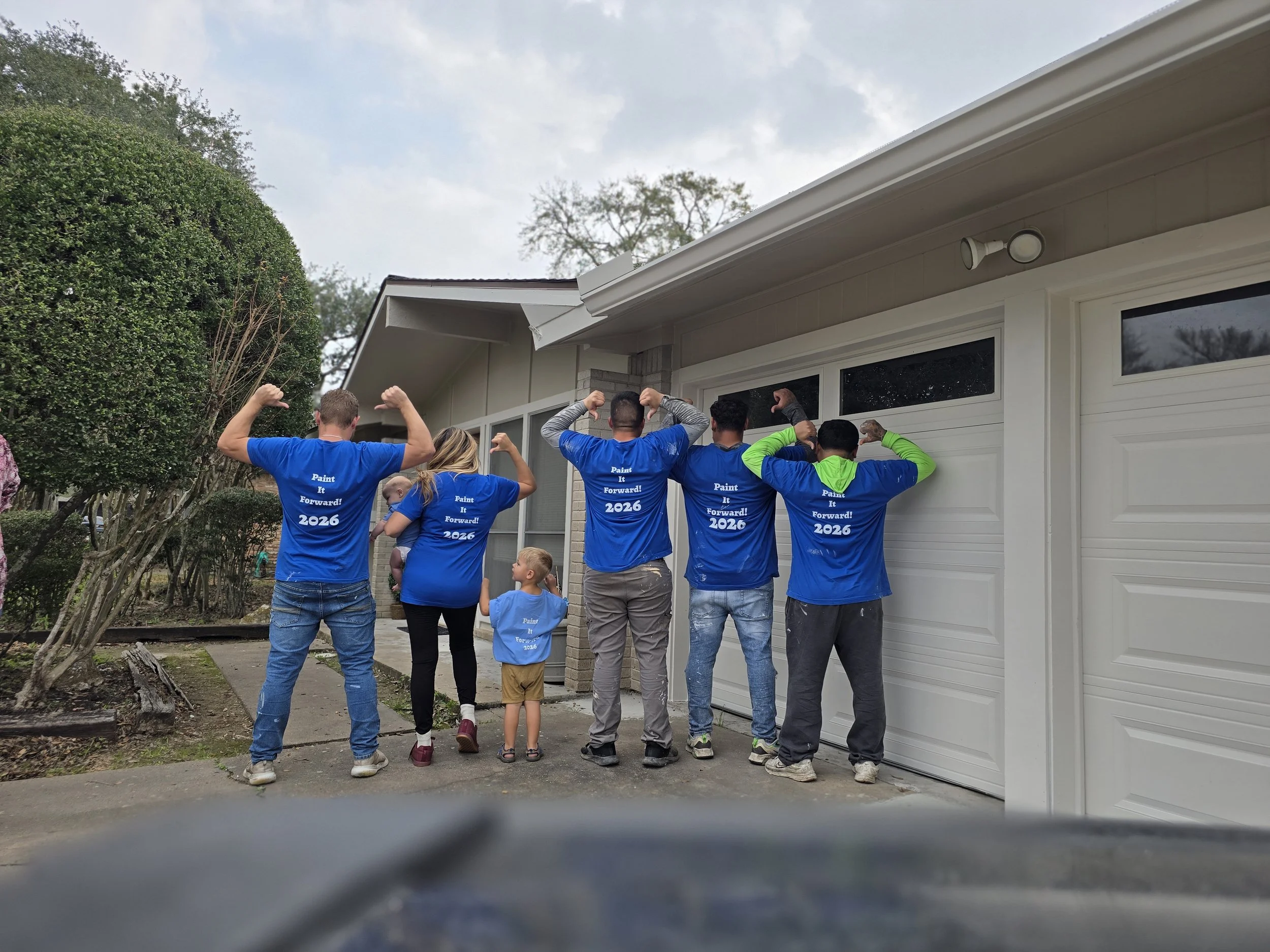 Chris and his painting crew standing together with his wife Sarah and children on the driveway of a home they are restoring in Sugar Land
