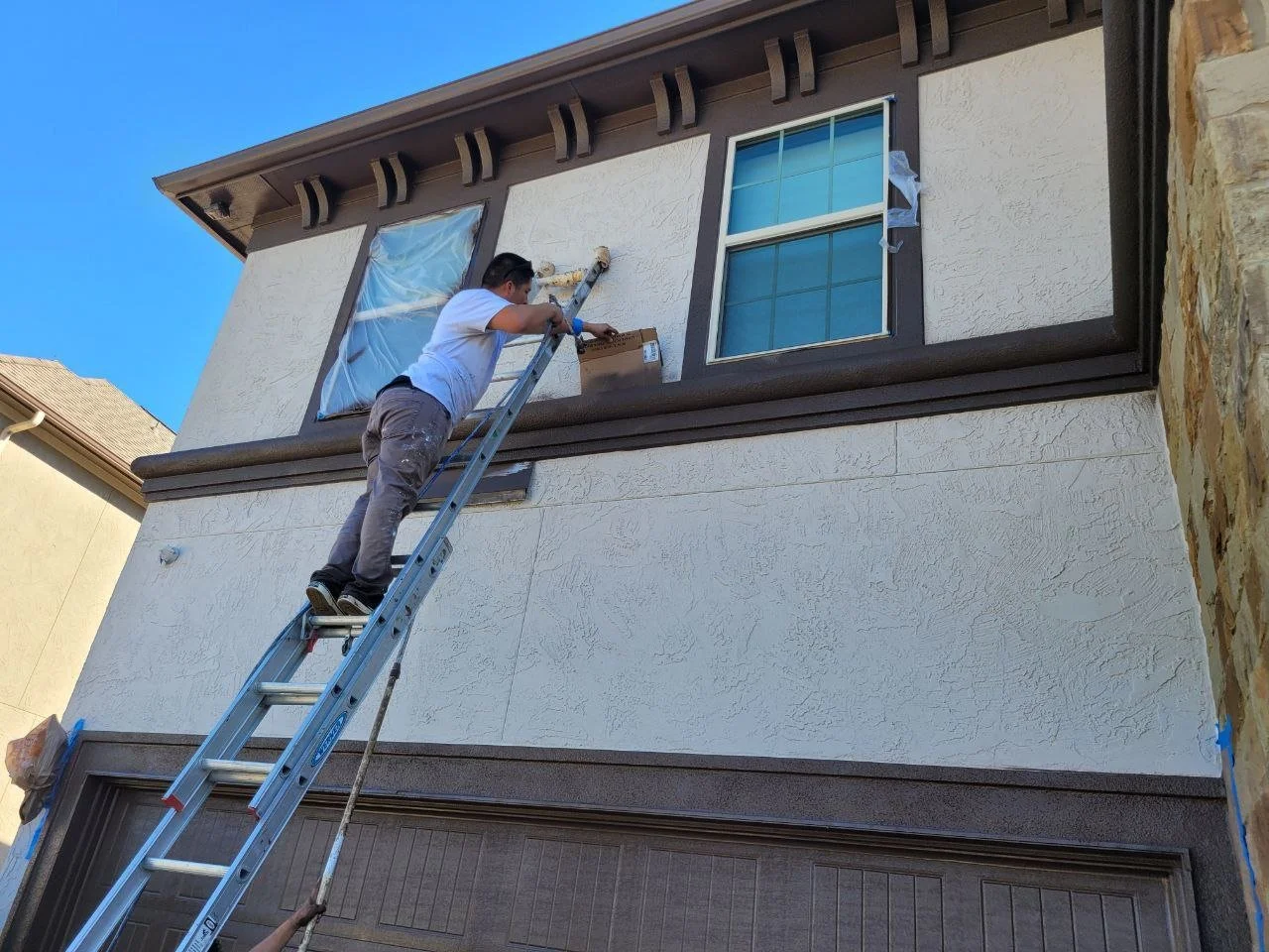 Two professional painters spraying a house exterior using masking shields to protect surfaces in Missouri City, Texas.