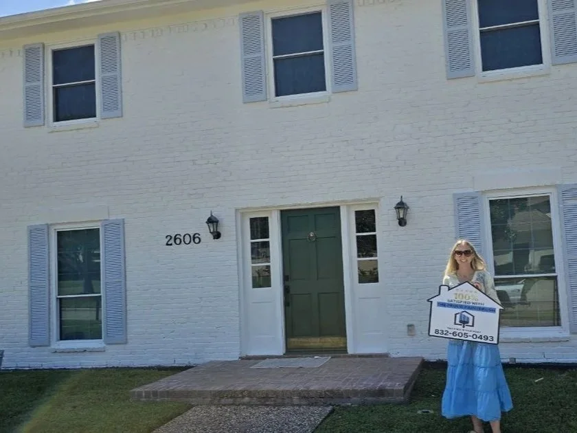 Freshly painted white brick exterior with blue shutters in Texas, featuring homeowner holding a “100% satisfied” sign.