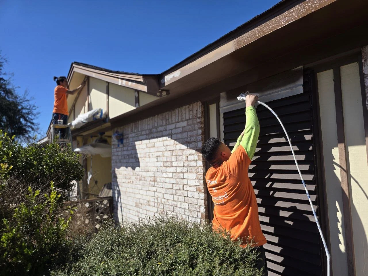 Two painters working on a small one-story house exterior