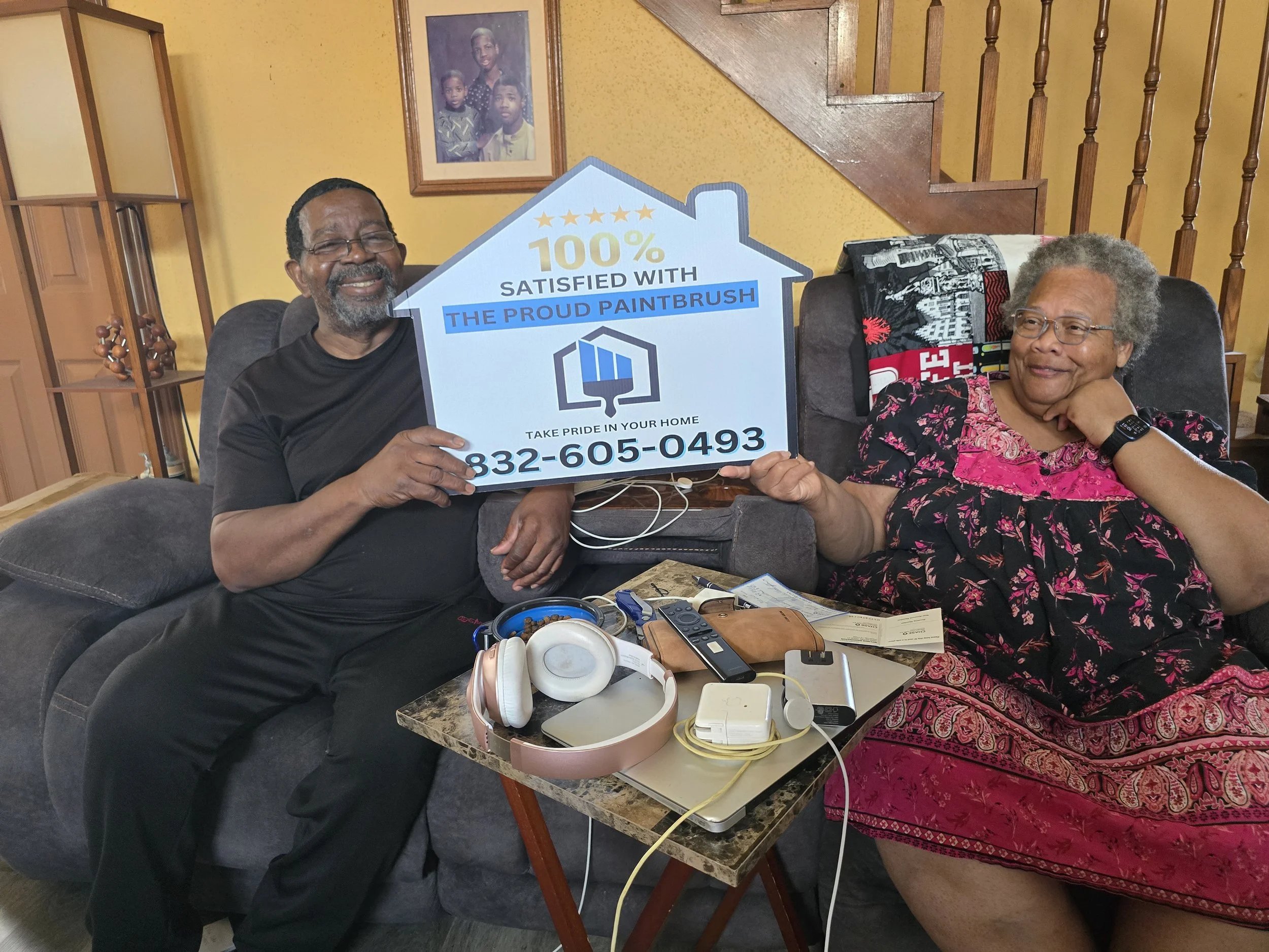 Smiling homeowners holding a 100% satisfied sign after a painting project by The Proud Paintbrush in West Houston, Texas.