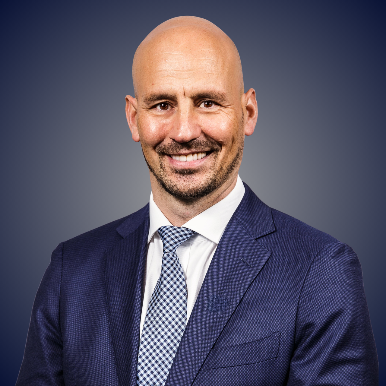 Et portrett av en smilende mann med rødt hår og skjegg, iført en svart polo-skjorte, mot en gradient bakgrunn.