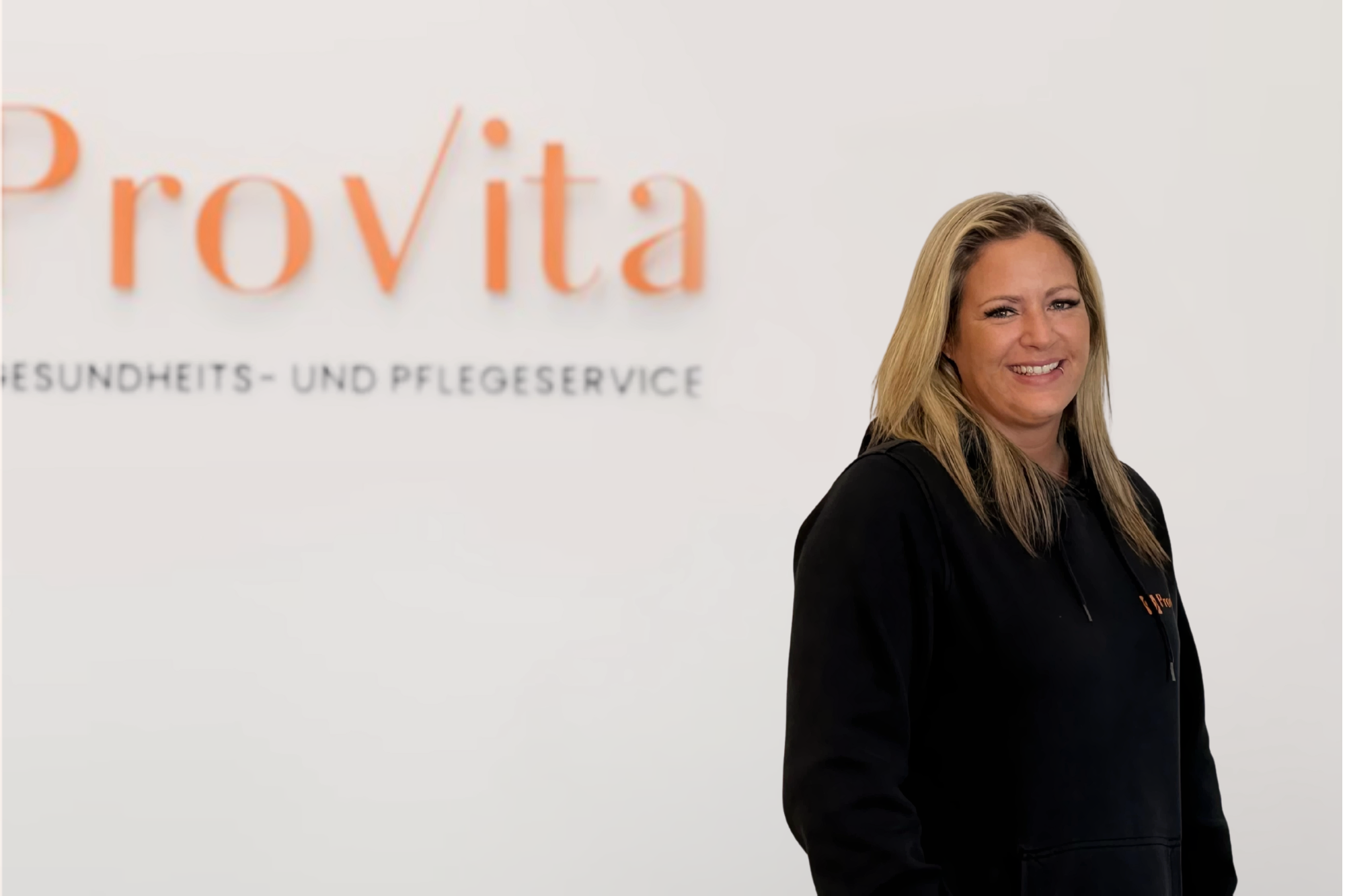 Mitarbeiterin von Provita Gesundheits- und Pflegeservice lächelt vor dem Unternehmenslogo – Vertrauen, Nähe und Kompetenz in der ambulanten Pflege.