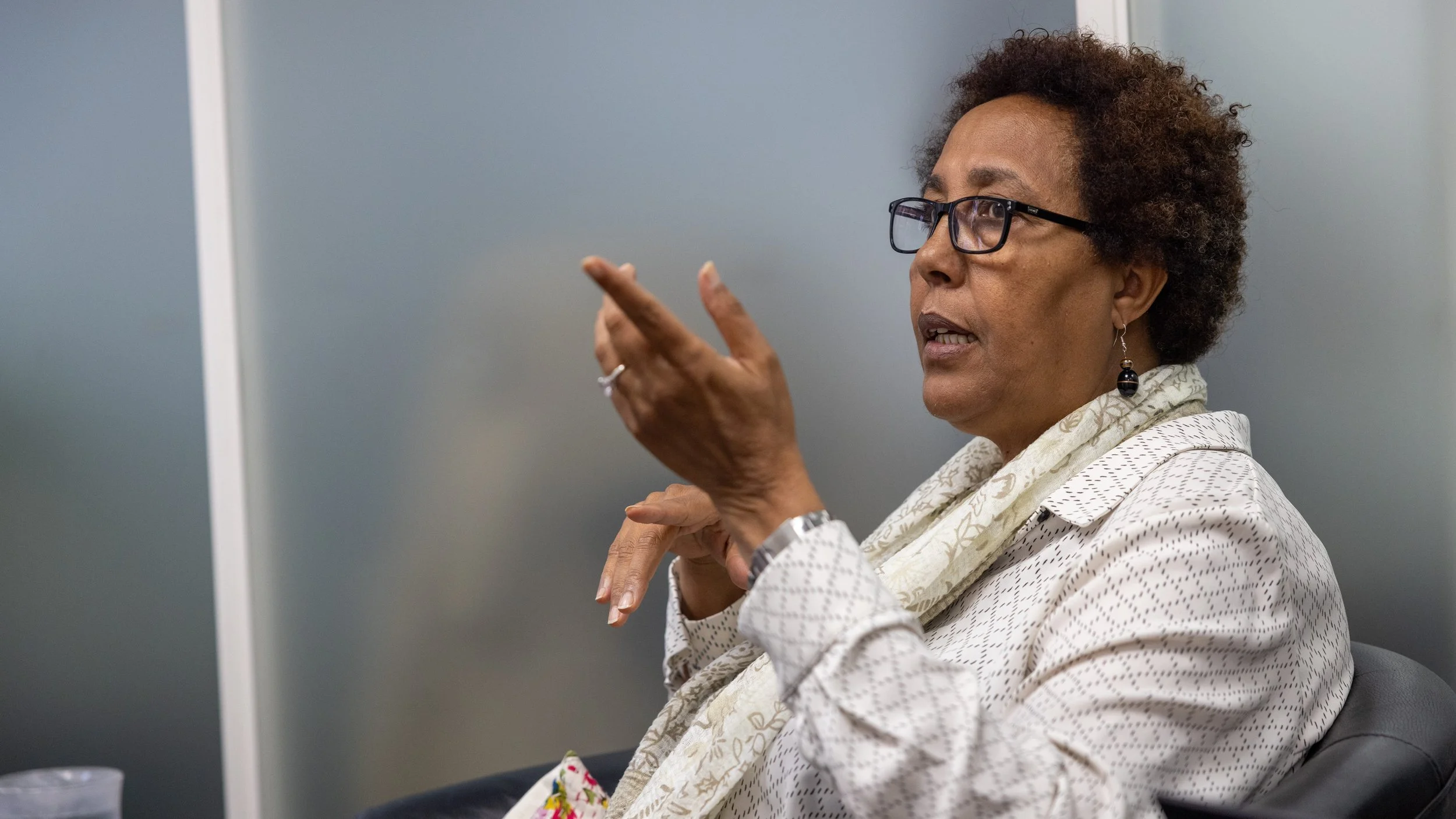 A woman with glasses and a purple scarf is speaking with a man.