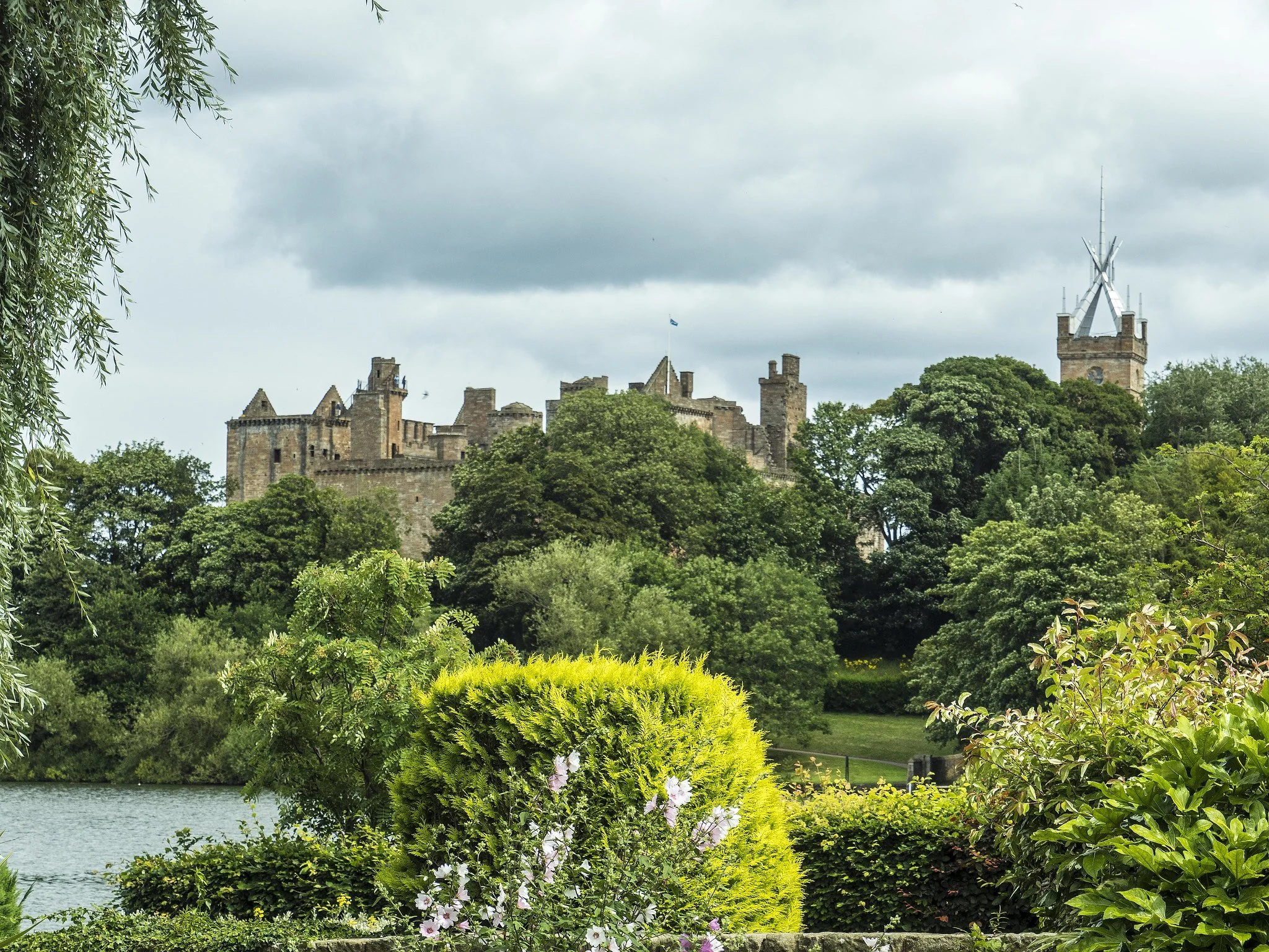 The tops of Linlithgow Castle peeking through the tops of the trees in front of the loch