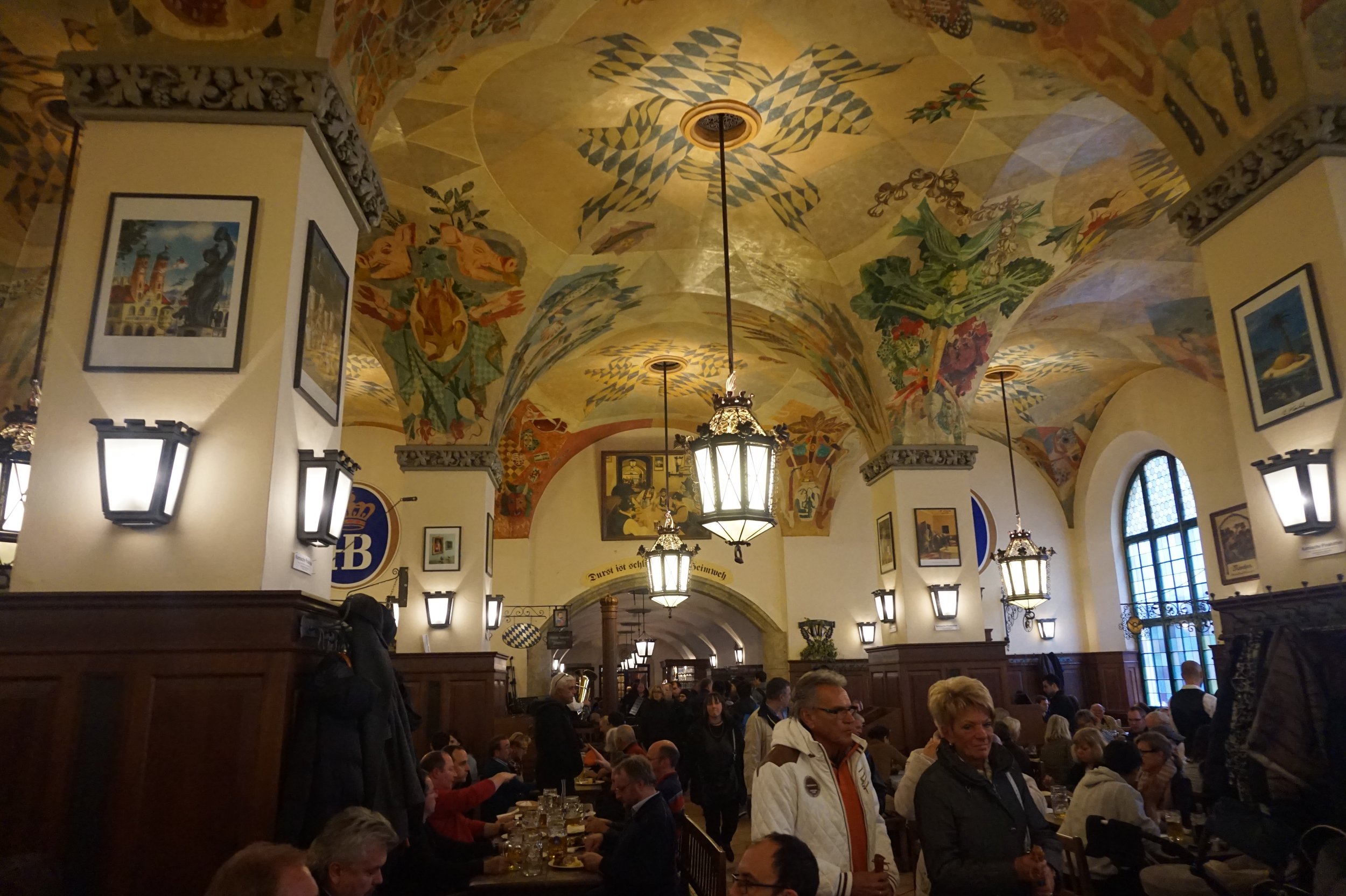 Crowded interior of the Hofbrauhaus with colorful paintings on the vaulted ceiling