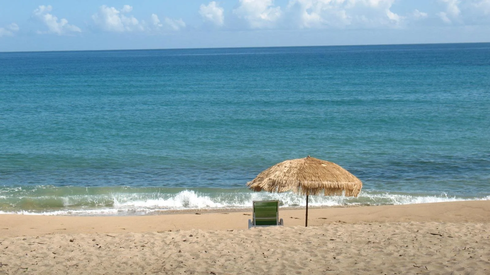 Beach chair with straw umbrella over it on the shores of Rincon