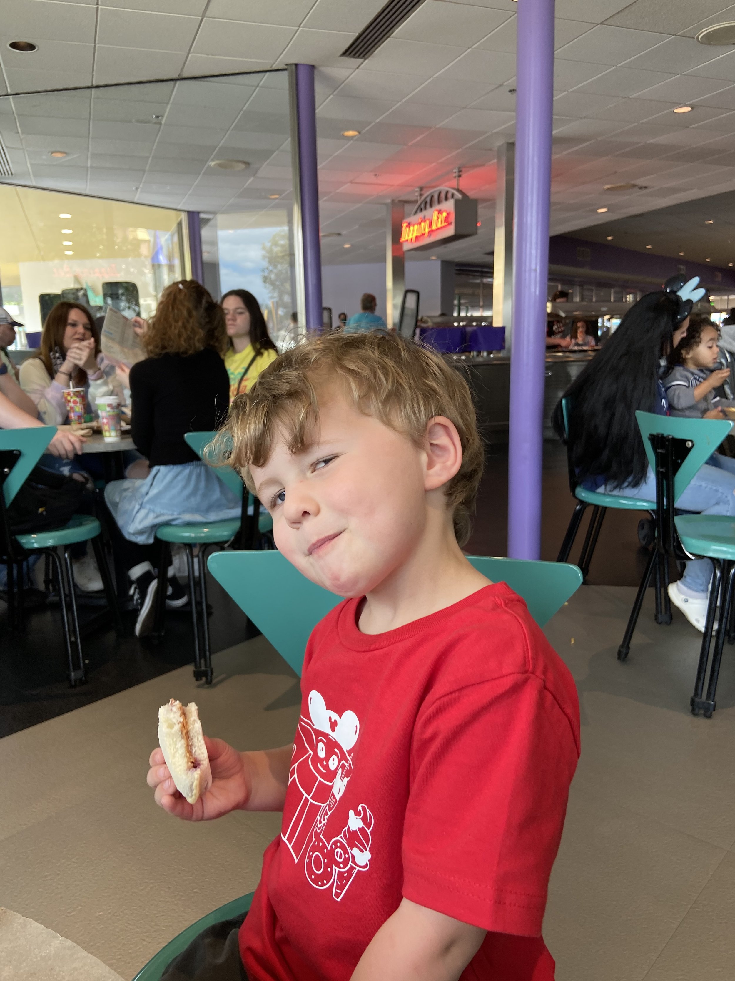 The author's son sits in a restaurant in Disney World holding an Uncrustables peanut butter and jelly sandwich