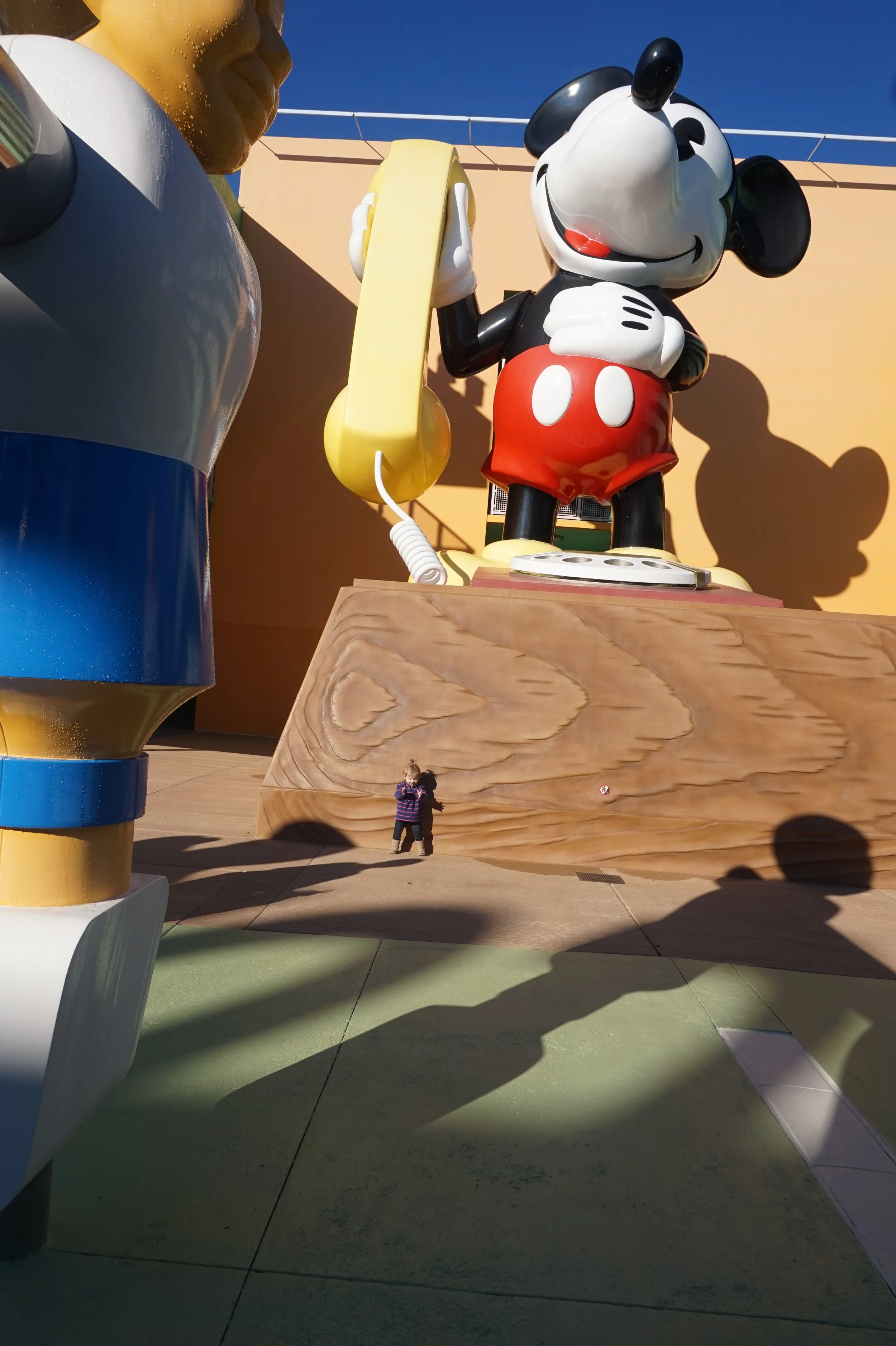 The author's daughter stands in front of a 2 story tall statue of a Mickey Mouse phone