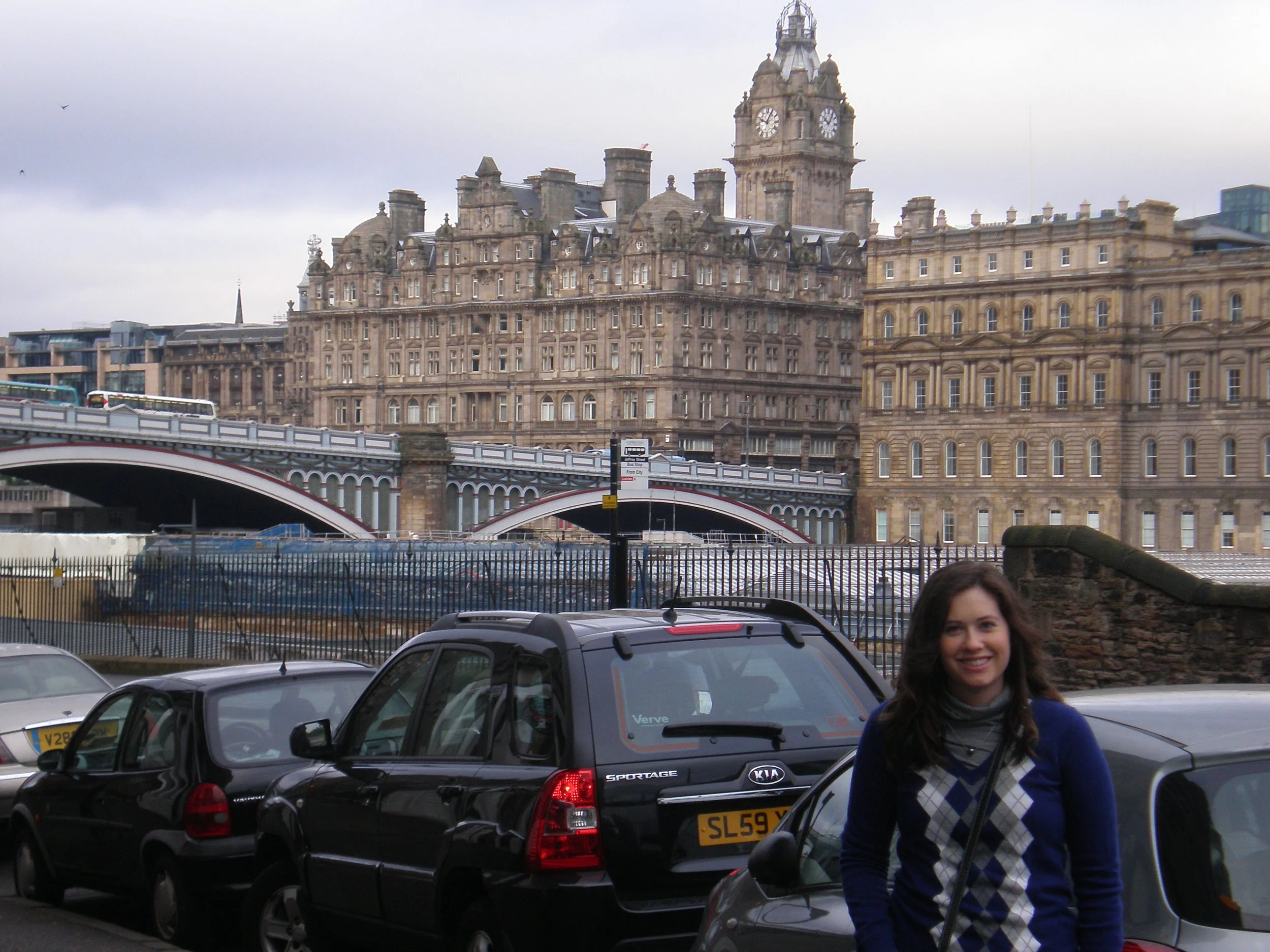The author stands in front of cars parked outside of Waverly Station with New Town in the background