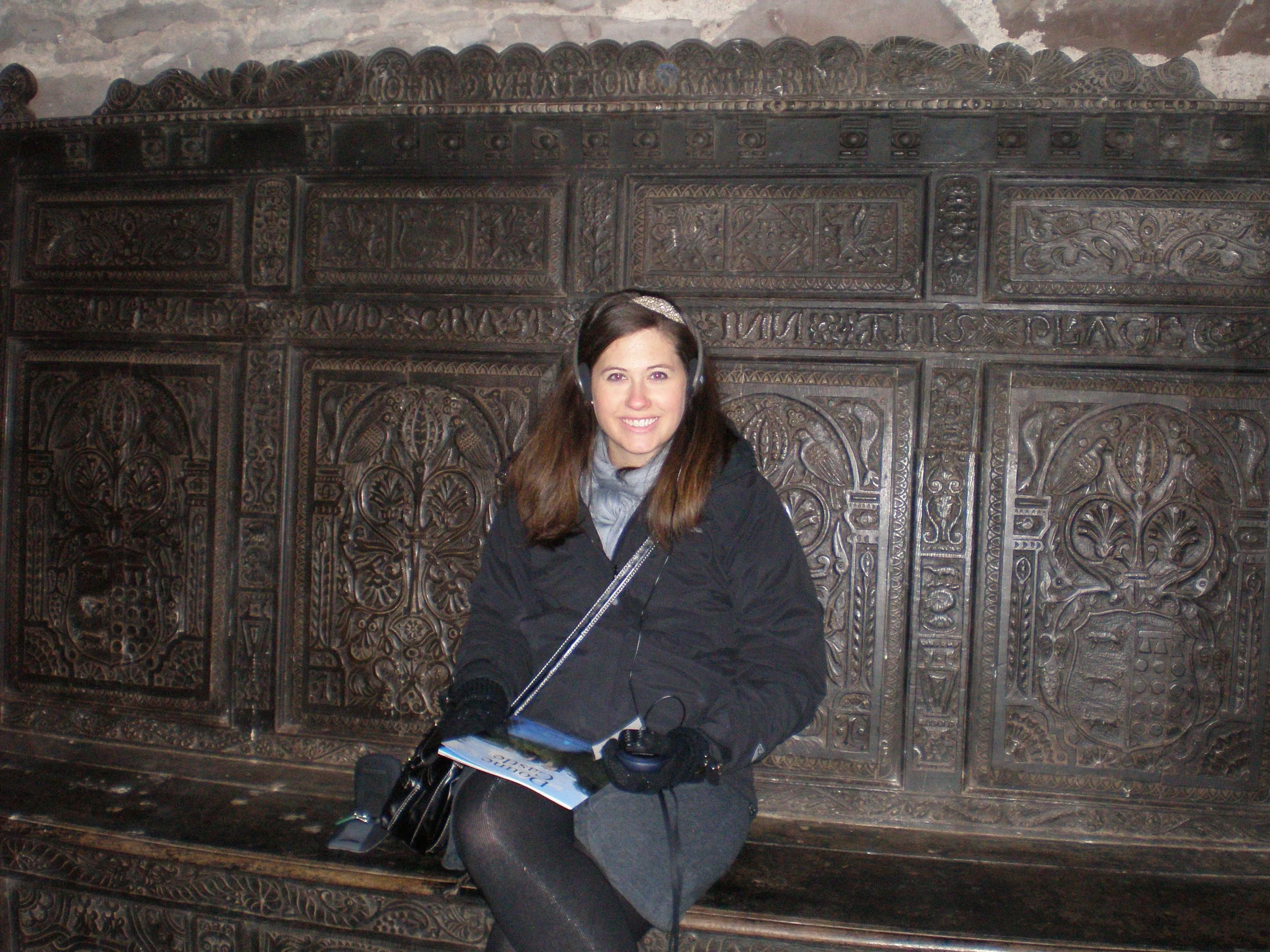 The author sitting on a wooden bench with intricate carvings in the Great Hall of Doune Hall with headphones on