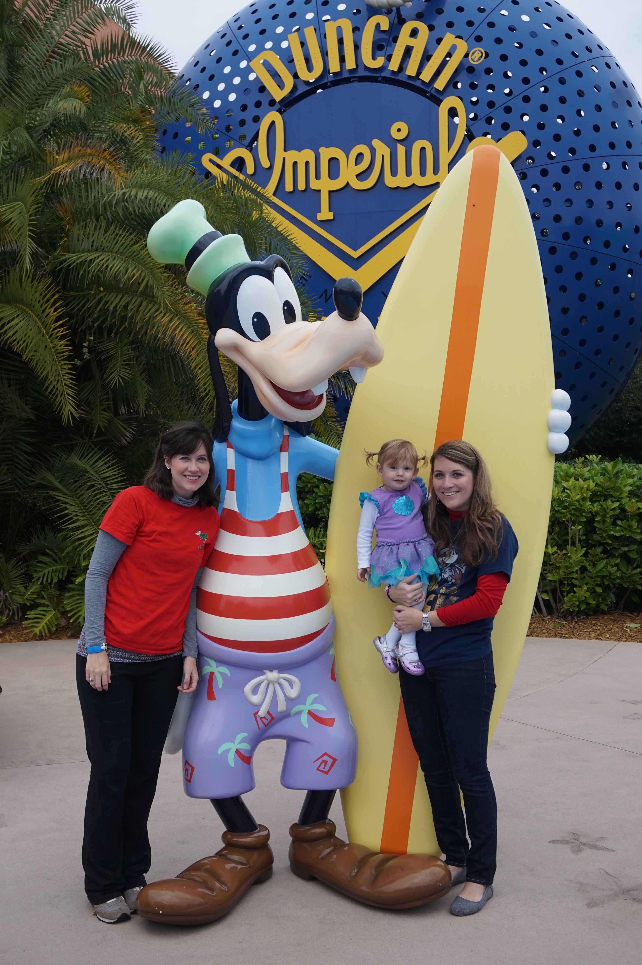 The author, her sister, and her daughter stand next to a large statue of Goofy holding a surfboard