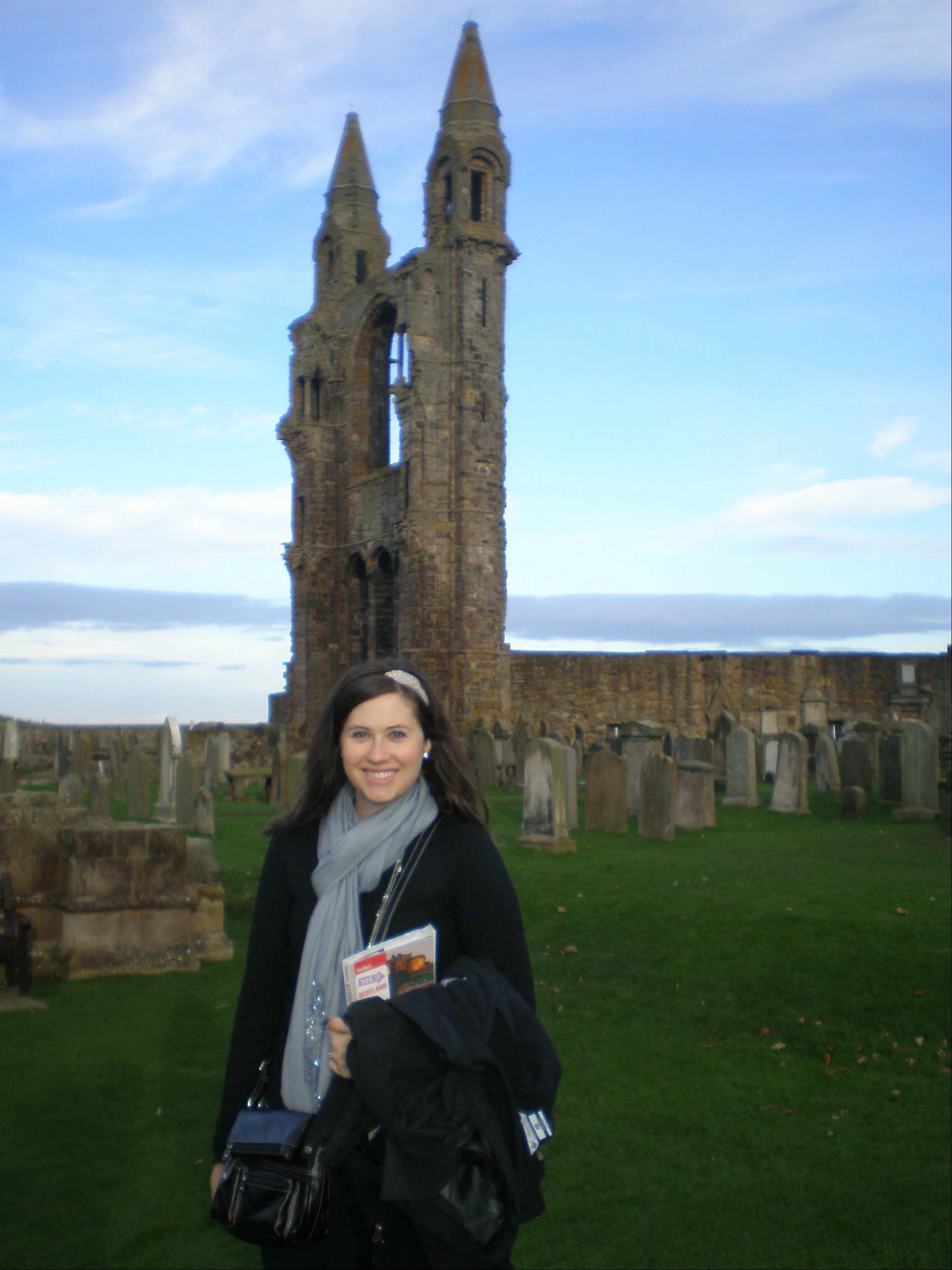 The author holding a guidebook and standing in front of the ruins of St. Andrews Cathedral