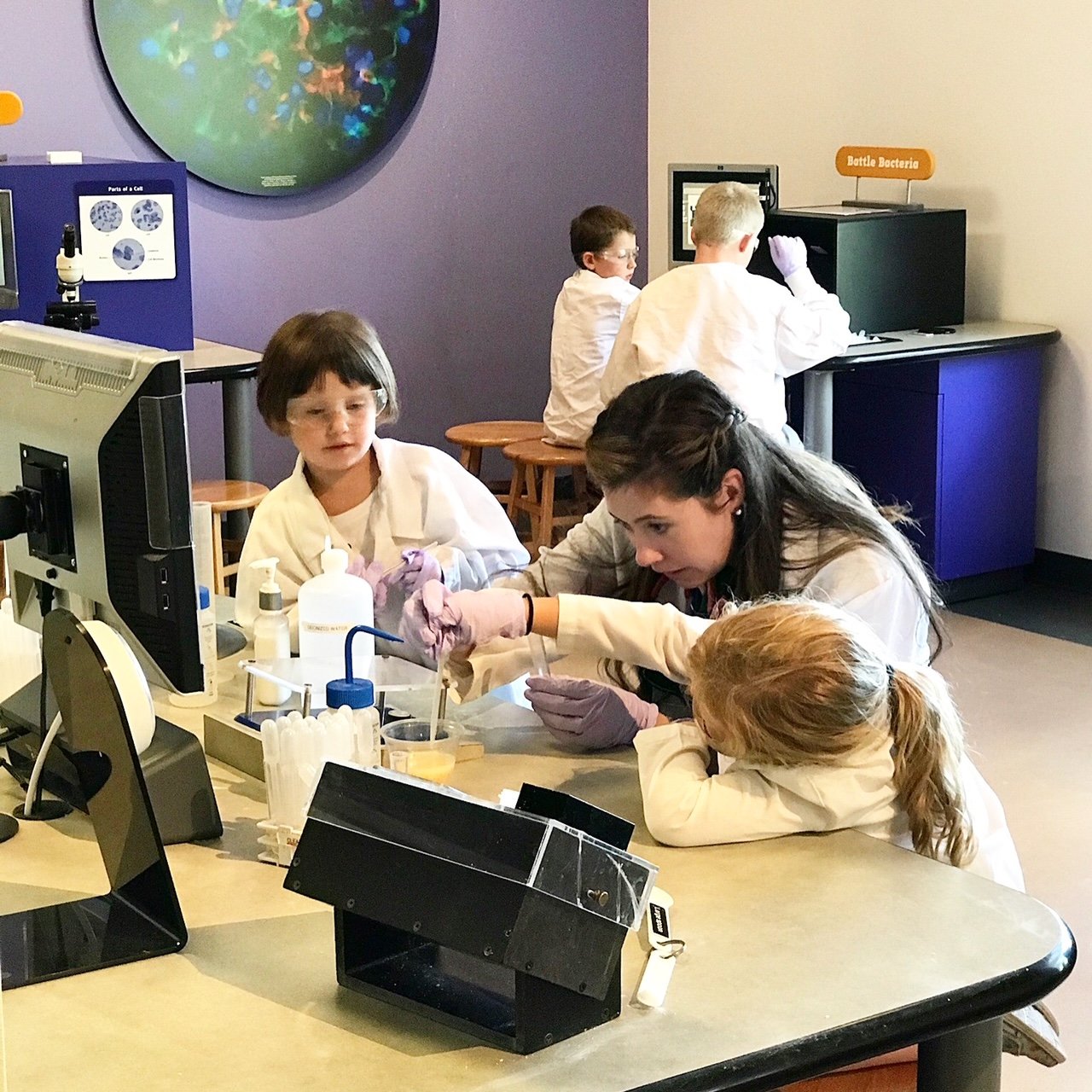 The author helps 2 young children with a science experiment at the Denver Museum of Nature and Science