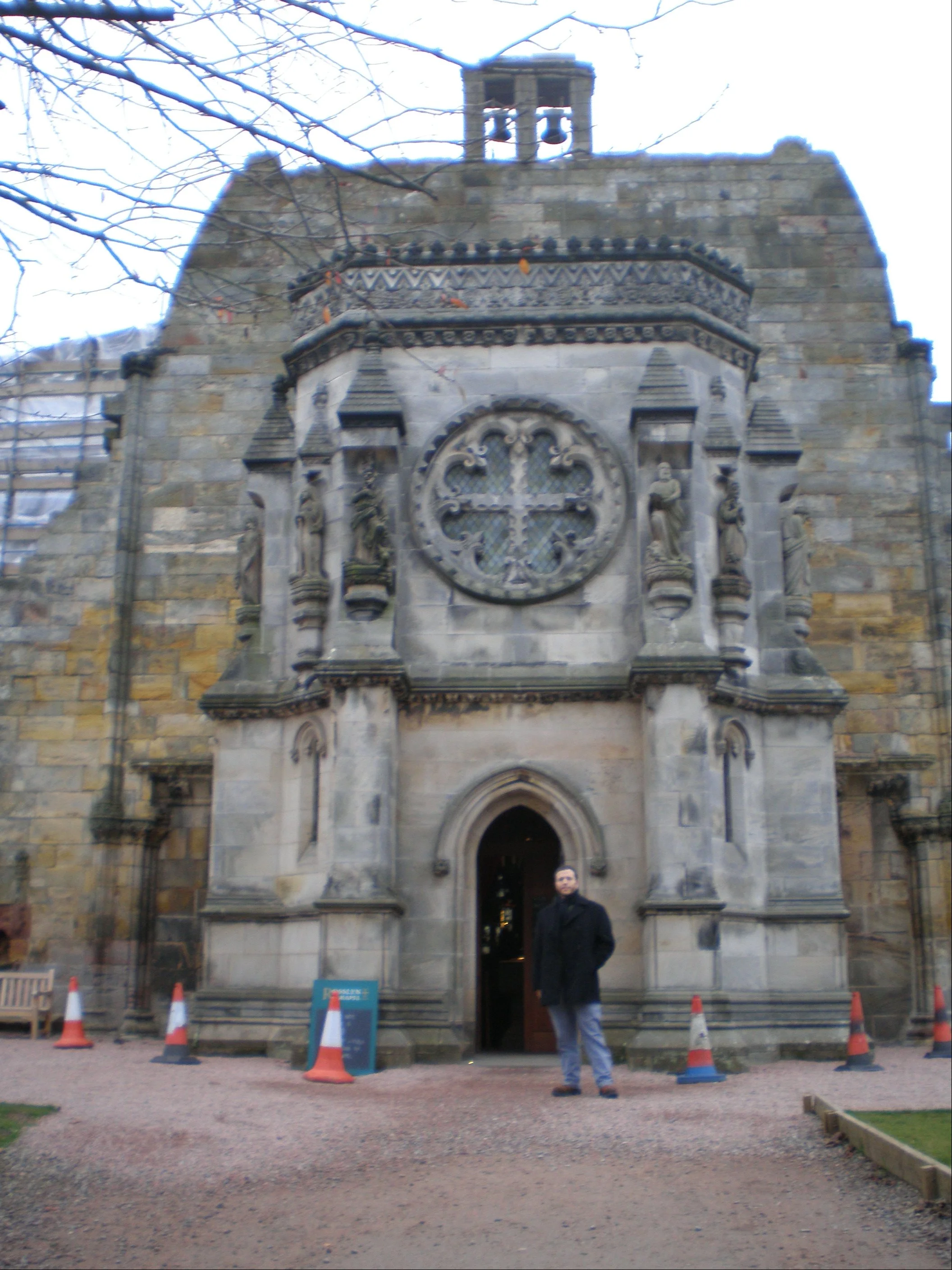 The author's husband wearing a black coat and standing in front of the visitors entrance to Rosslyn Chapel