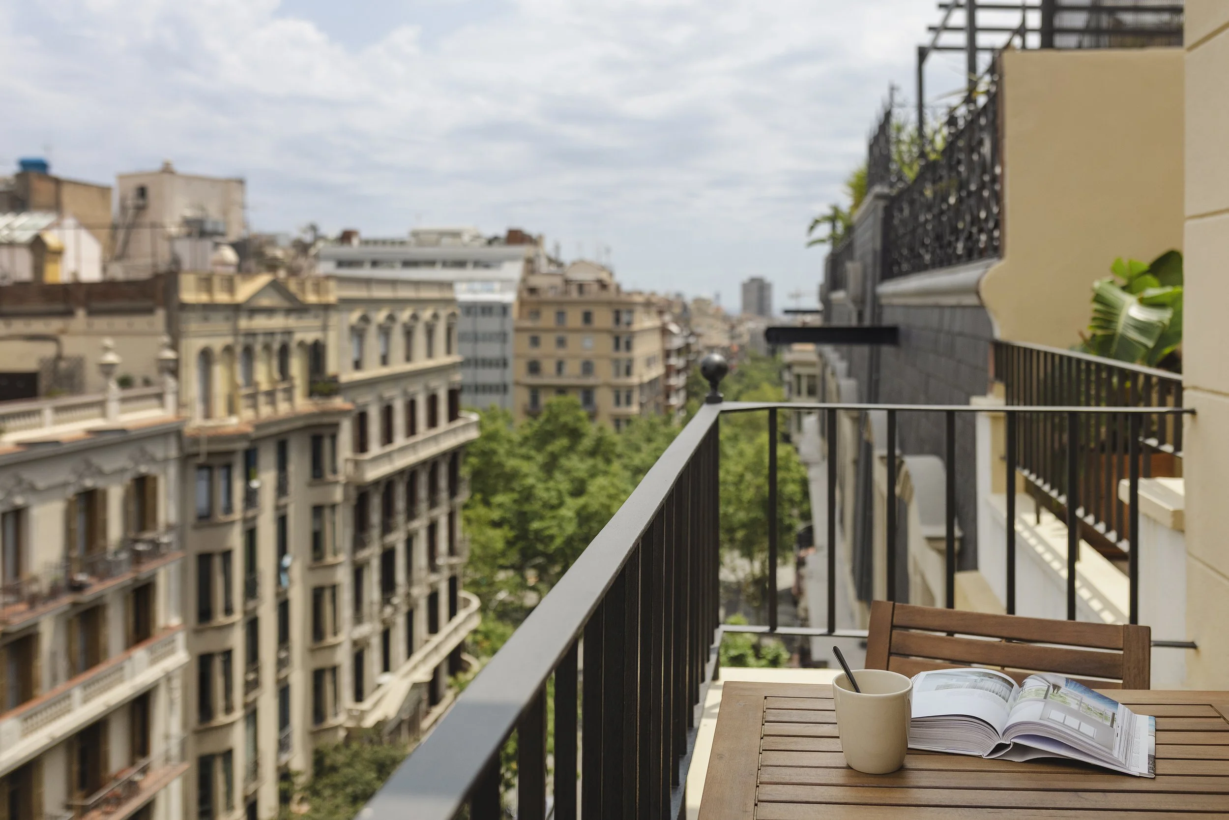 Vista desde el balcón de los edificios de la ciudad con una mesa que tiene una revista, una taza con una cuchara y una silla.