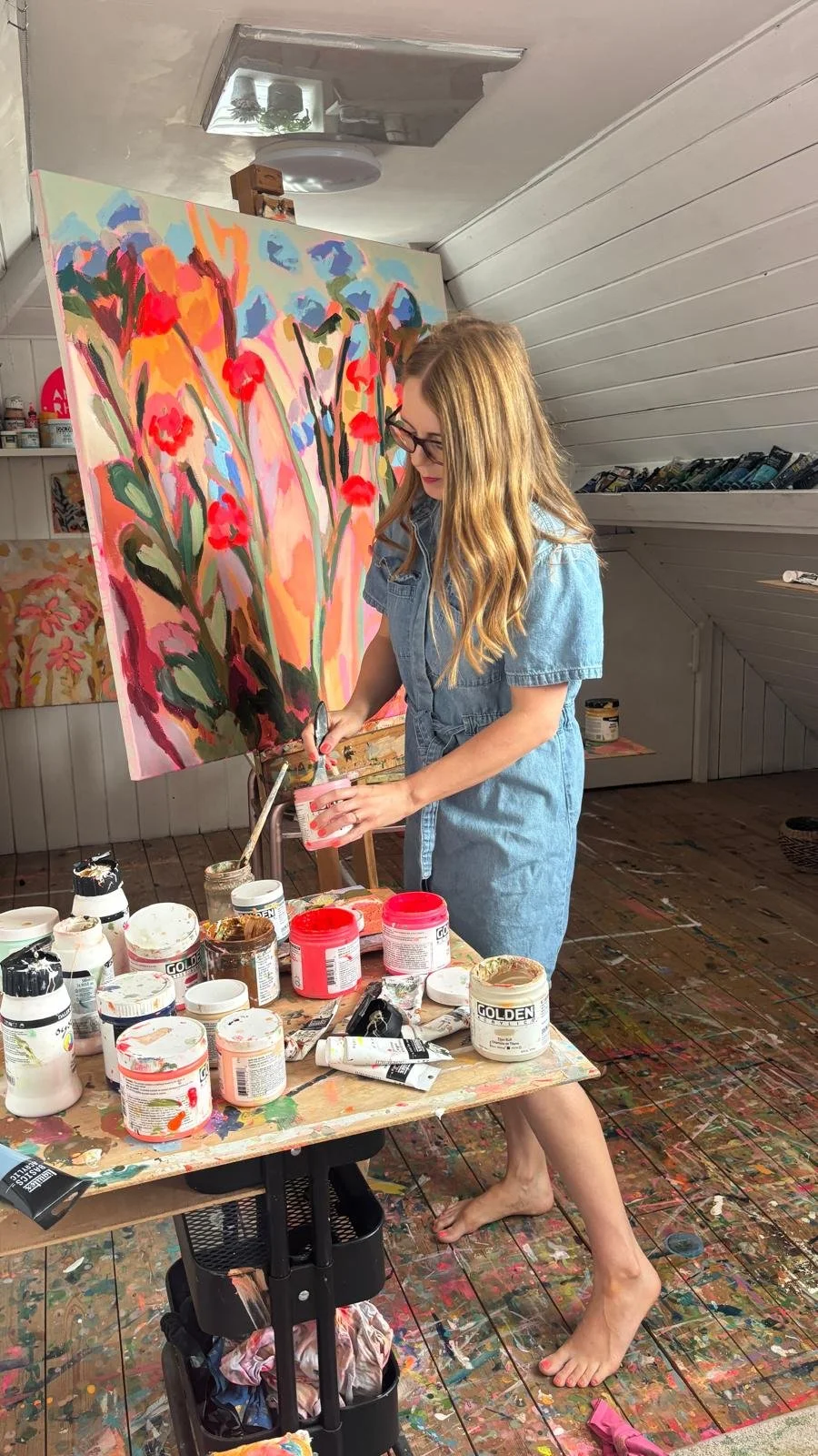 British artist Amy Rhodes in her Staffordshire studio with bright vibrant colourful floral painting on the easel