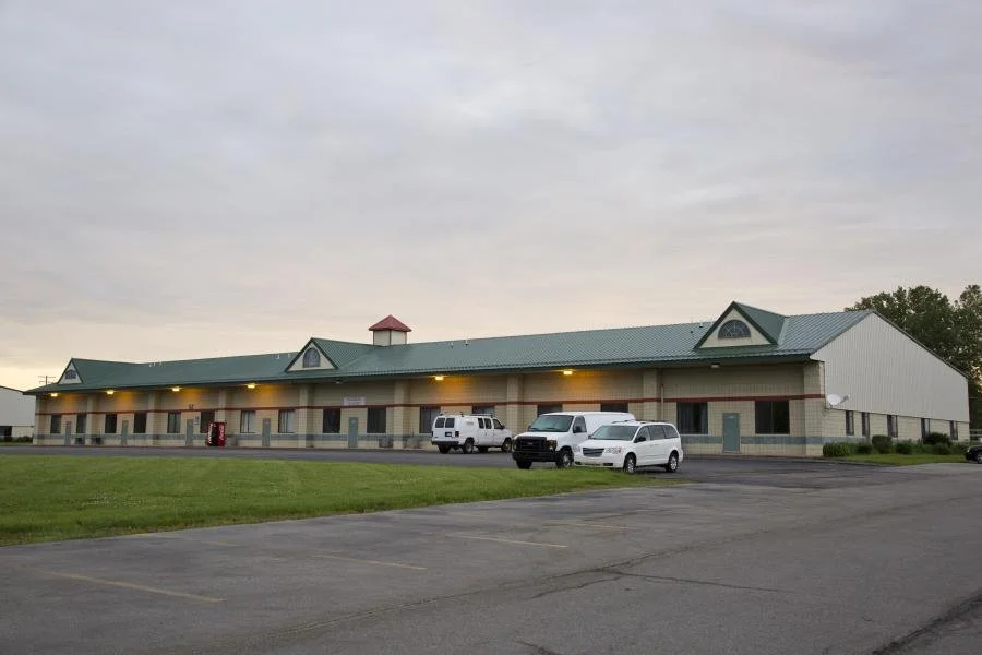 Long low commercial building with a covered walkway and parked vans at dusk