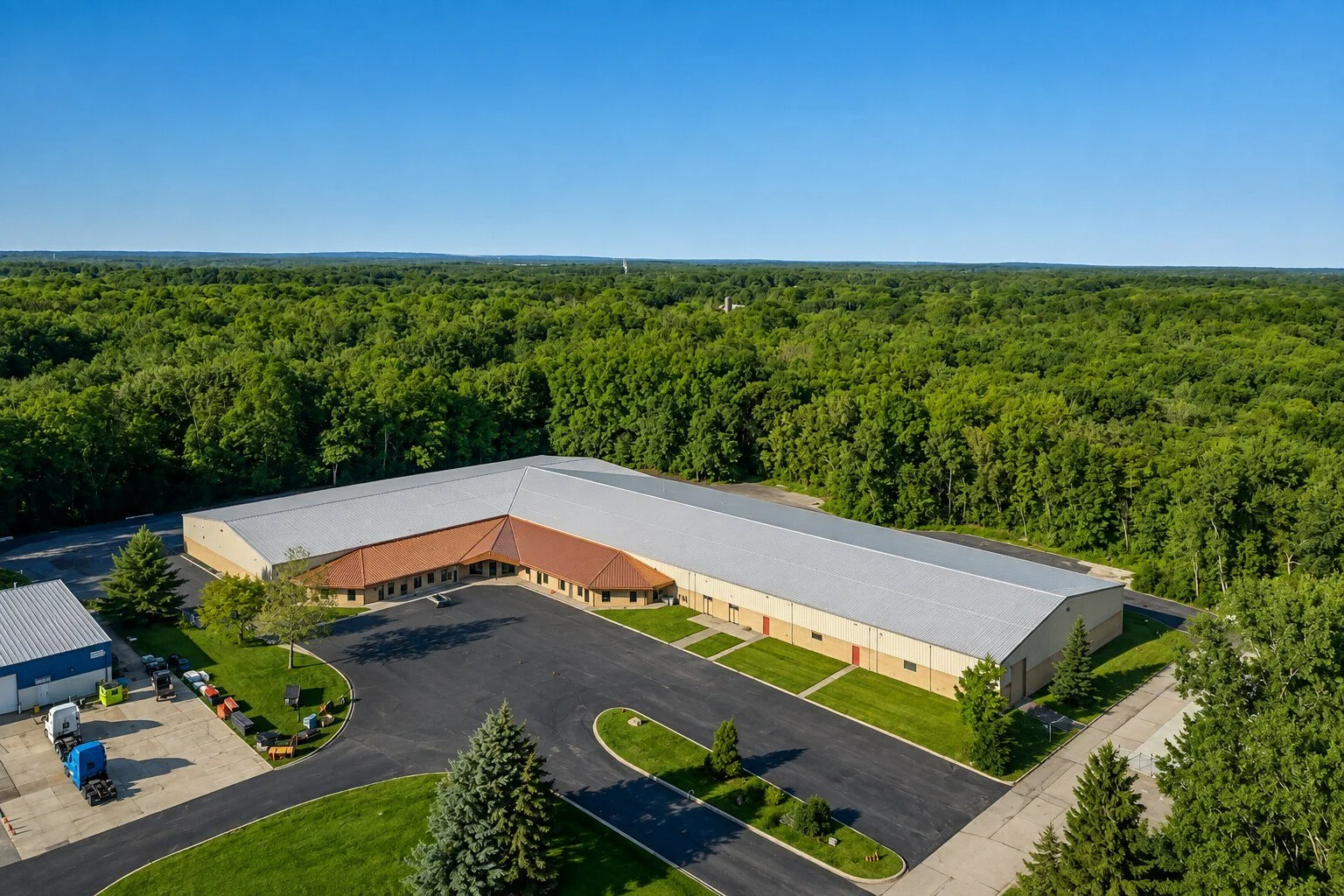 A large commercial building with a parking lot surrounded by green trees and a clear blue sky.