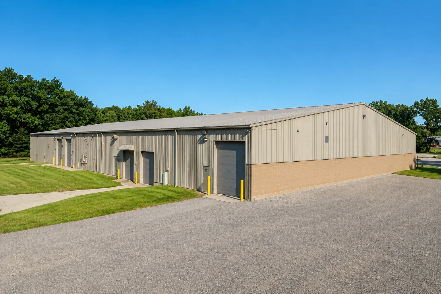 Large industrial storage building with multiple garage doors, metal siding, and a paved area in the foreground under a clear blue sky.