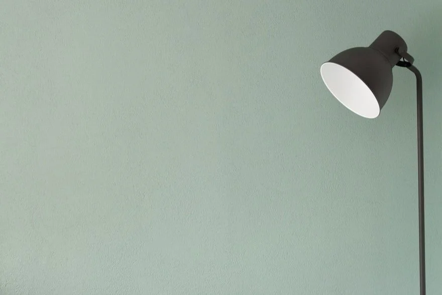 Minimalist desk lamp against a soft green background, representing focus and intentional use of time.