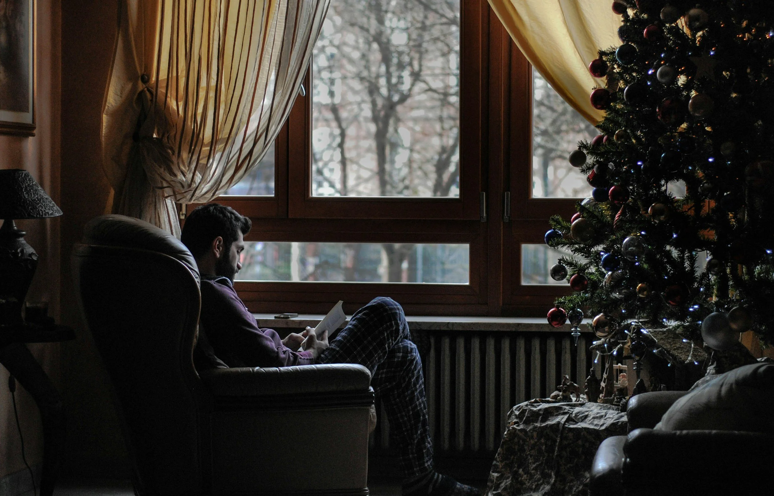 Man relaxing with a book beside a Christmas tree, symbolizing a peaceful and meaningful holiday spent on your own terms.