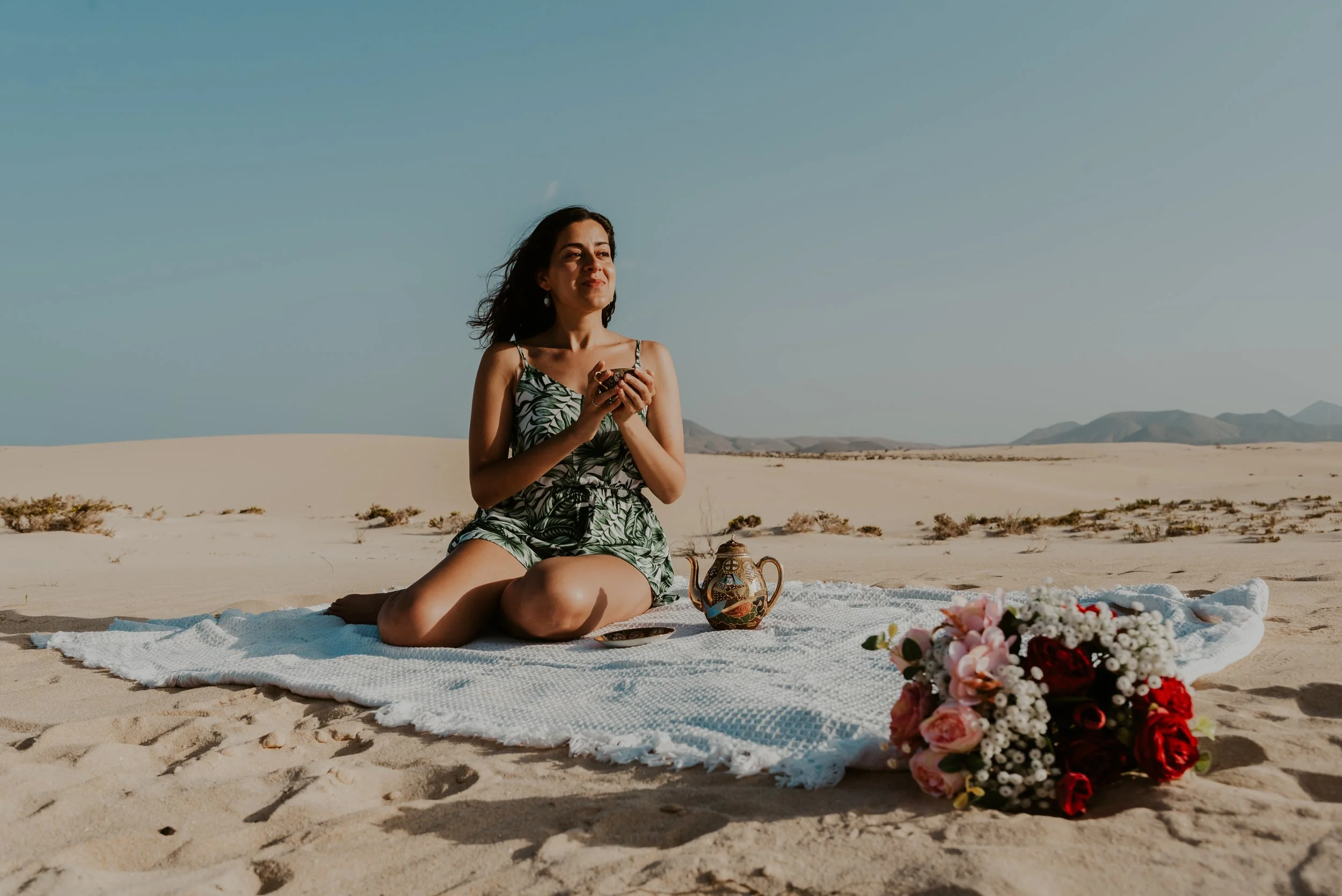 Carolina sitting peacefully on a beach with a cup of tea, surrounded by sand and nature, reflecting on personal priorities, values, and the life she wants to create.