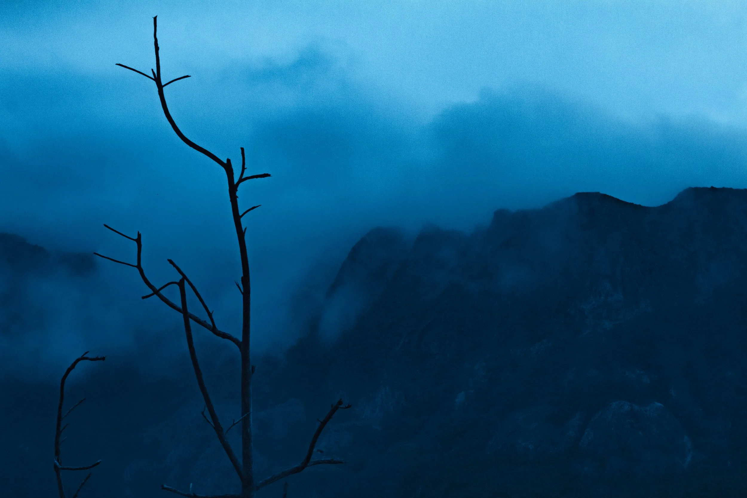 Paysage rocheux de l'île de Ua-Pou aux Marquises, baigné dans une lumière crépusculaire teintée de bleu. Photographie issue du projet "Retiens le bleu" d'Edwina Bellahouel, développé dans le cadre du mentorat photo en ligne de Préludes Photo.